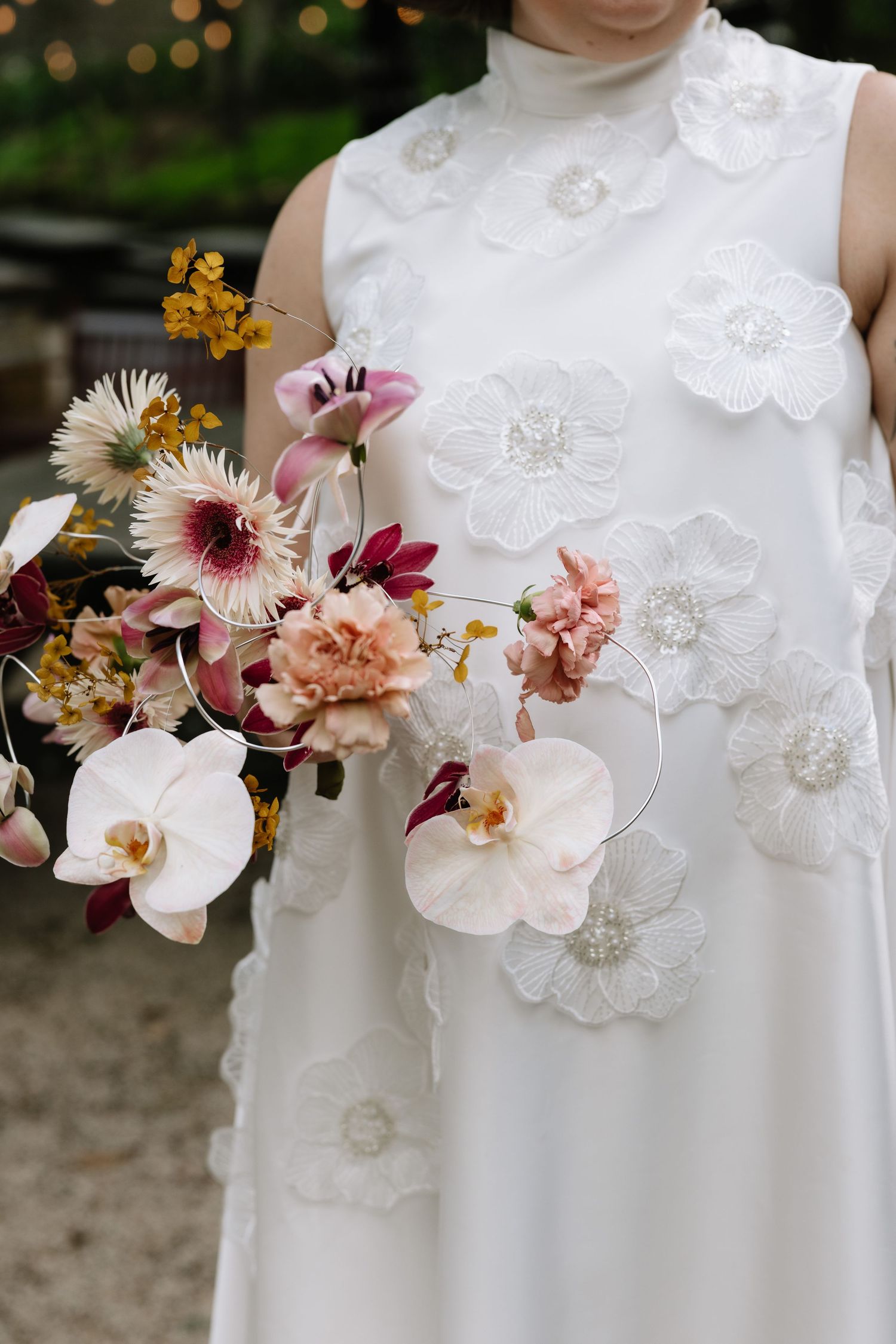 Bride in white floral appliqué gown holding a romantic bouquet of orchids, pink blooms, and burgundy flowers.