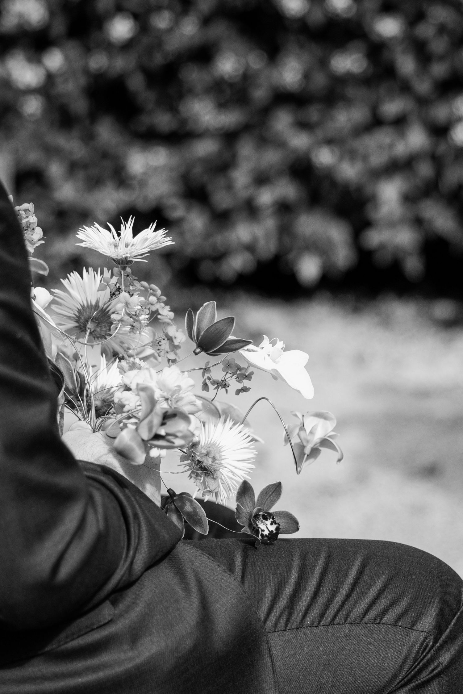 Black and white photo of a person holding a bouquet of flowers outdoors.