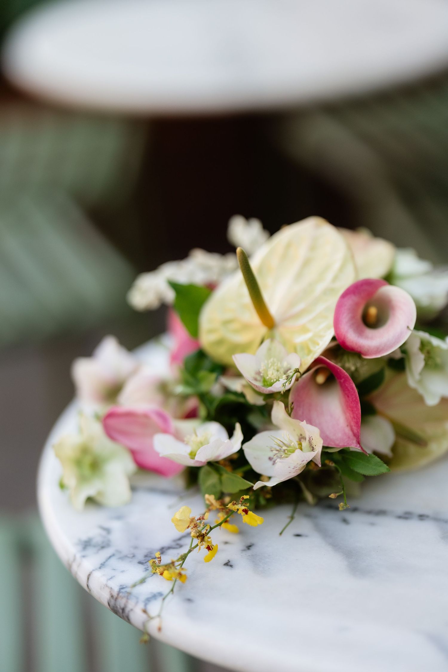 Elegant wedding bouquet with pink calla lilies and white flowers arranged on a marble table.
