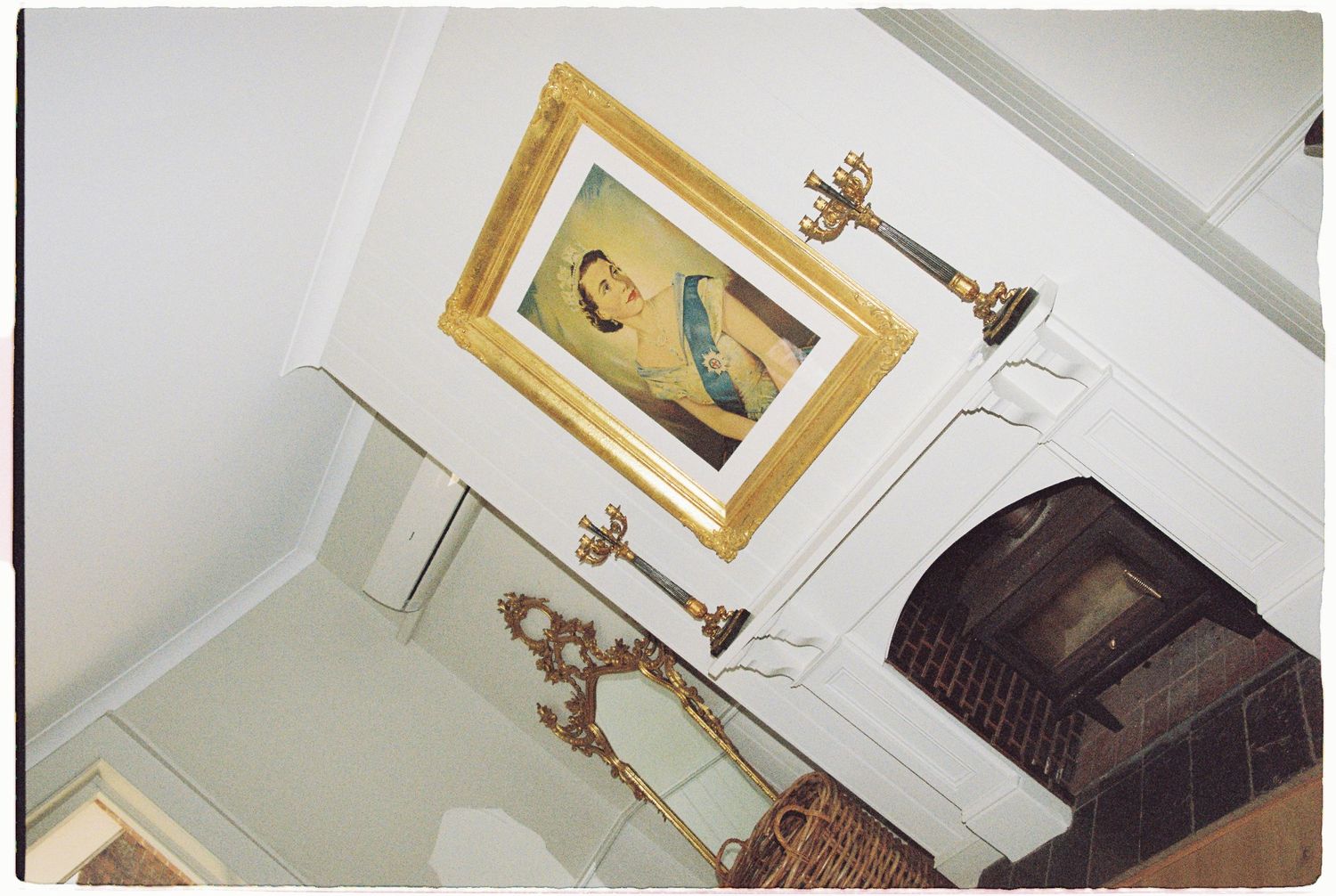 Angled interior shot of elegant room with gold-framed portrait above ornate fireplace.