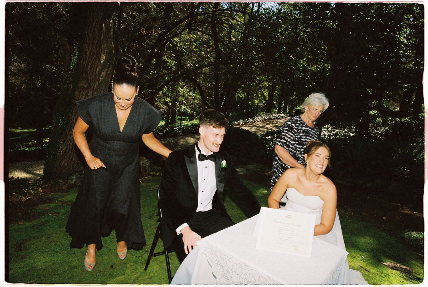 Wedding guests laughing and celebrating at an outdoor garden reception table.