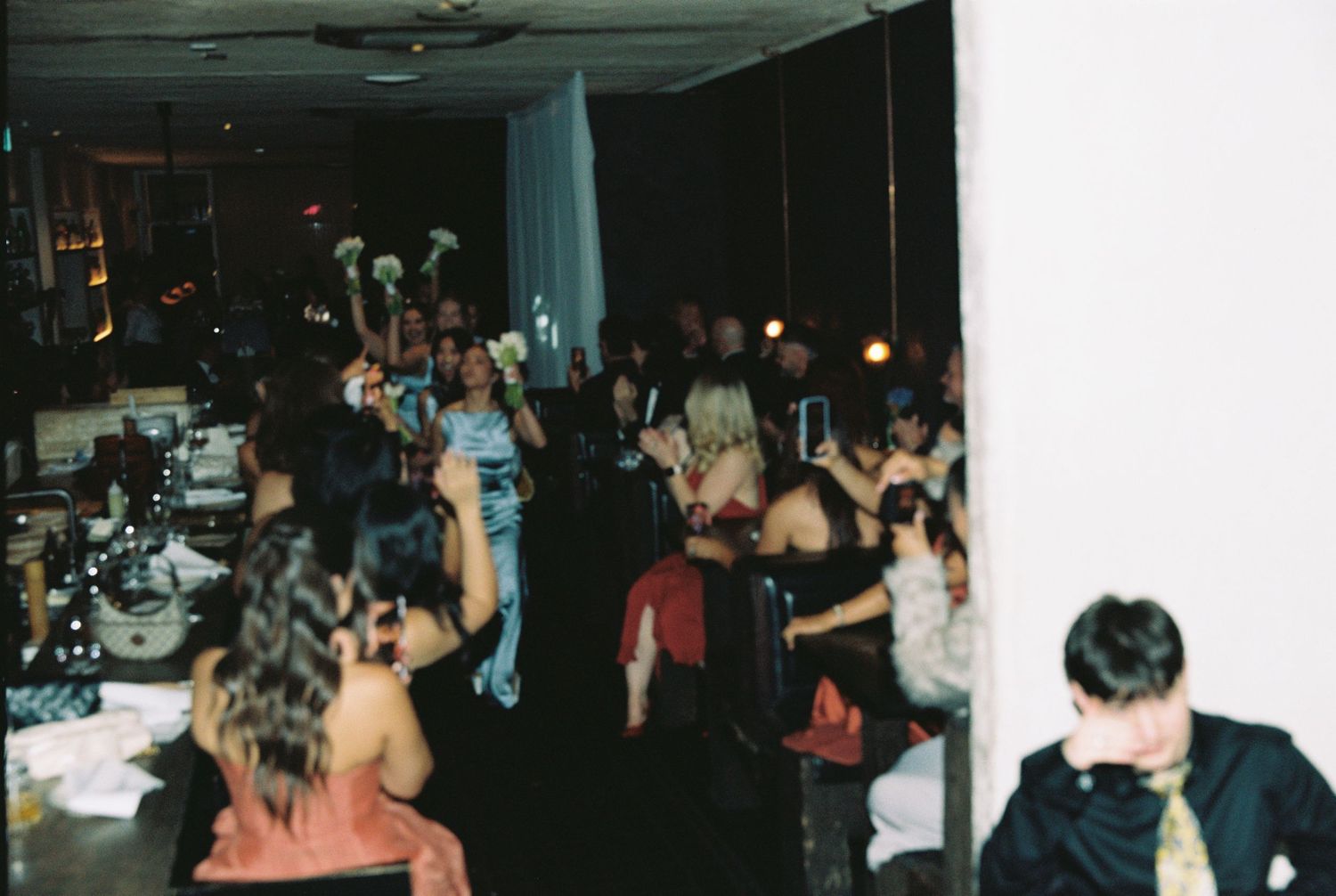 Guests celebrate and dance at a lively wedding reception with dim lighting.