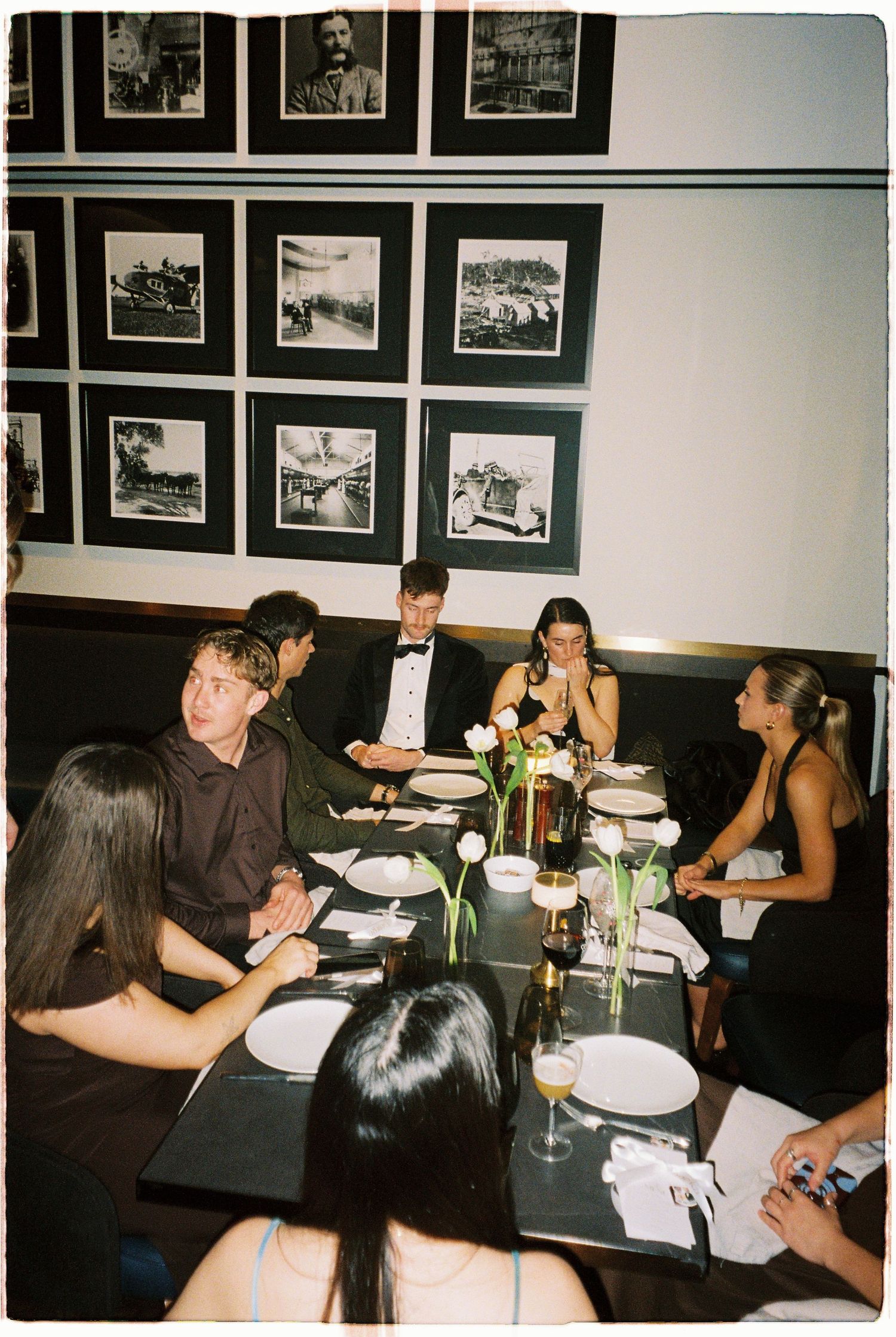 Wedding guests in formal attire dining at a restaurant table adorned with white tulips.