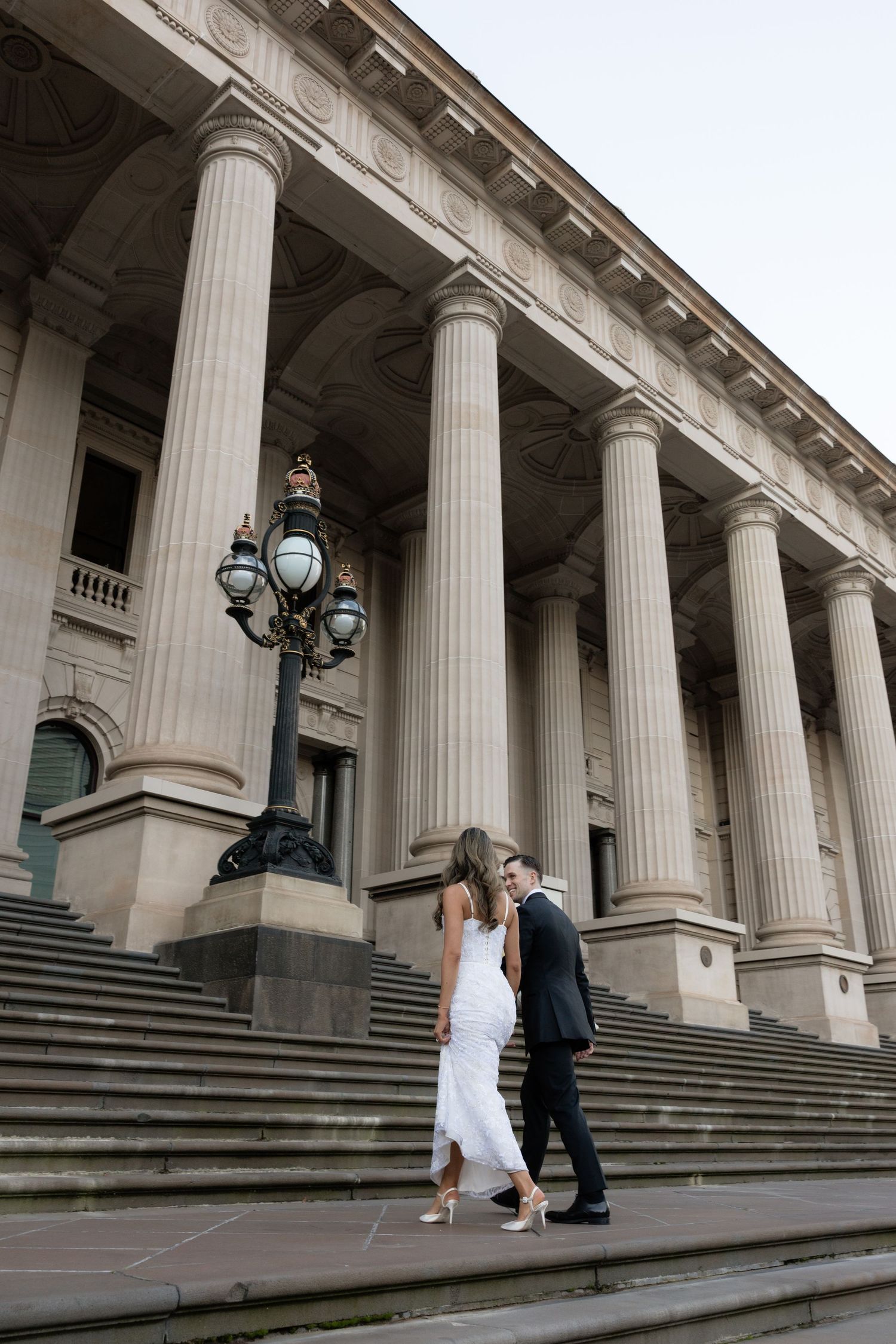 Bride and groom walking up grand stone steps with tall columns at Melbourne's Parliament House.