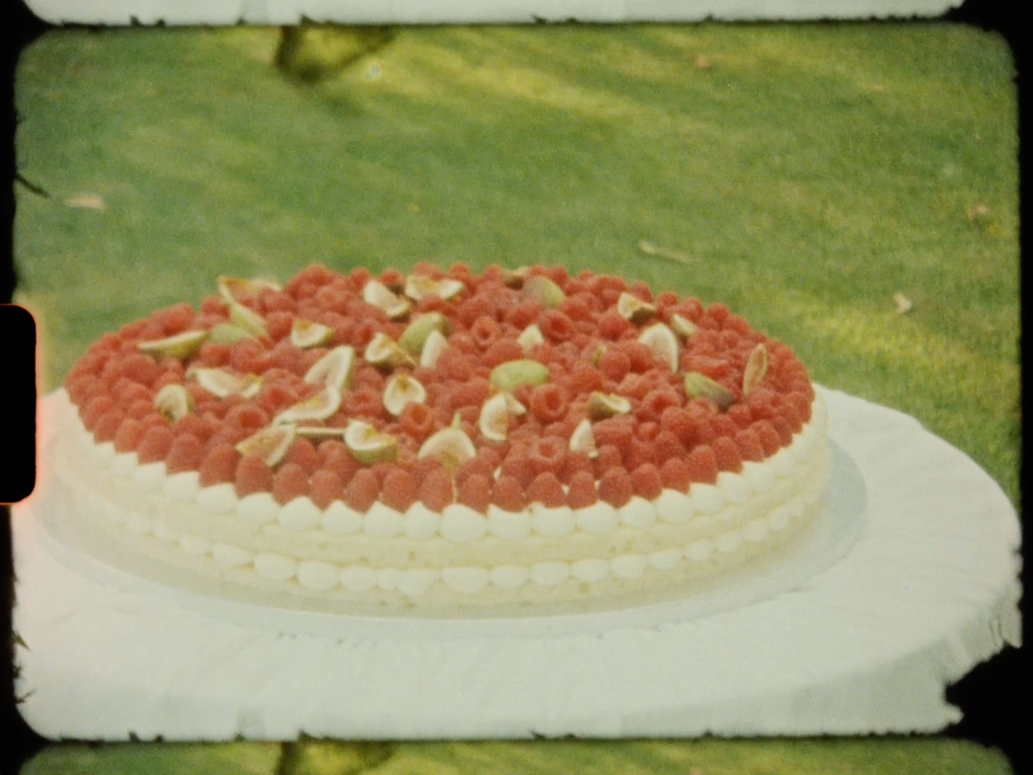 Round wedding cake decorated with fresh raspberries and white flowers on grass display.