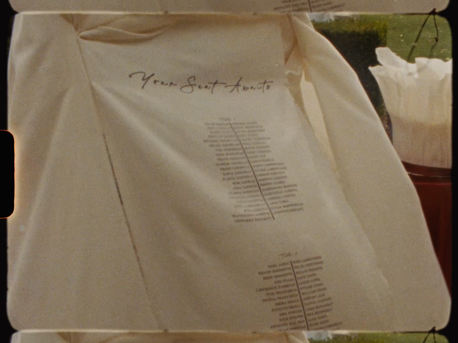Elegant handwritten wedding seating chart displayed on cream fabric for an outdoor garden reception.