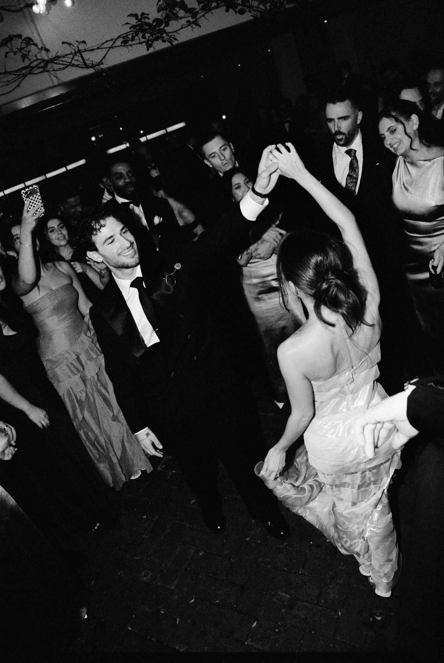 Bride and groom dancing joyfully at wedding reception surrounded by guests in formal attire.