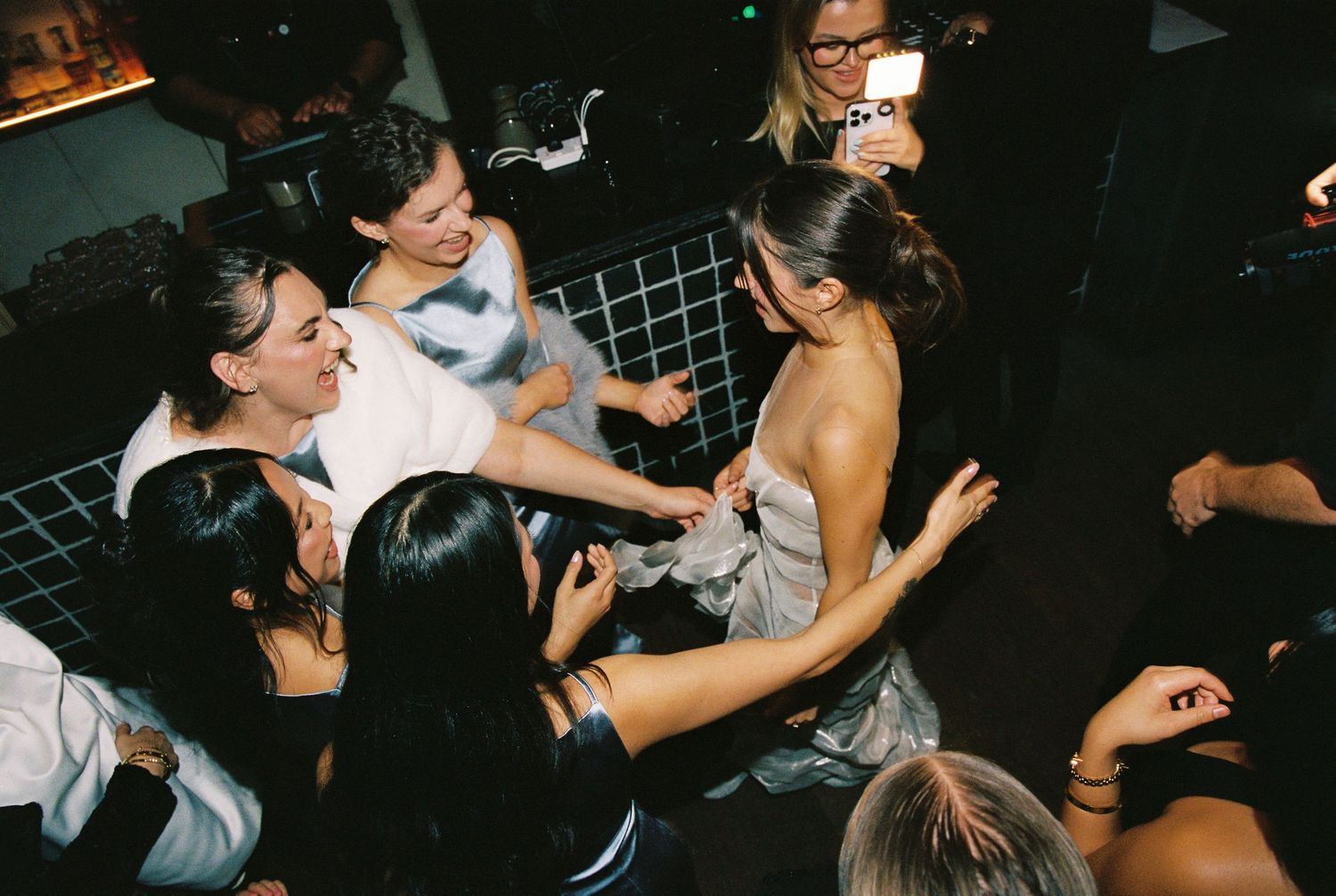 Bride surrounded by friends sharing a joyful moment on the dance floor.