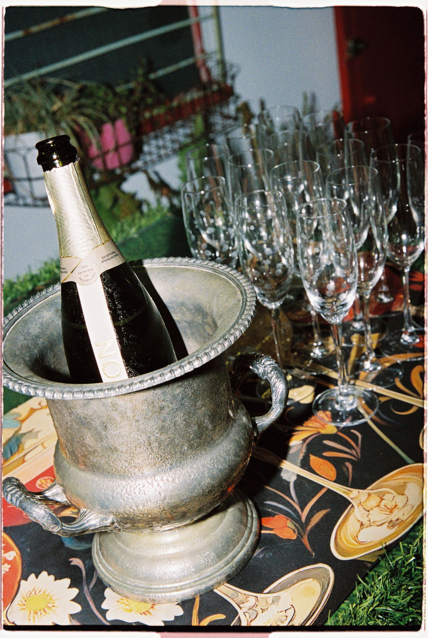 Champagne bottle chilling in silver ice bucket with crystal flutes on floral tablecloth.