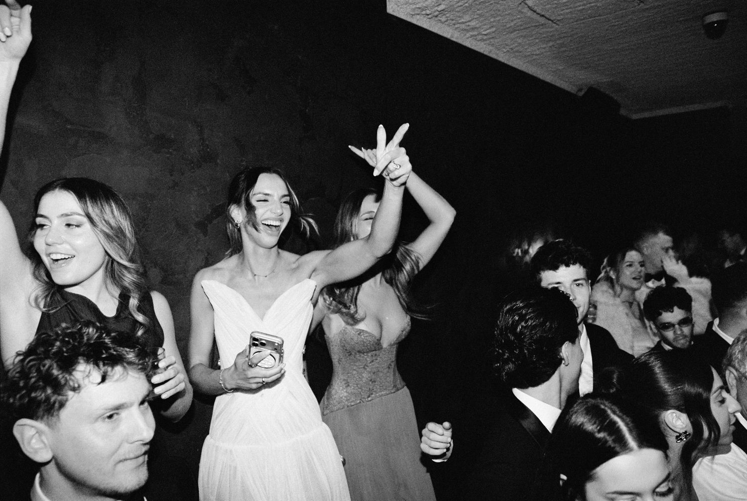 Black and white photo of a bride dancing joyfully with guests at a lively wedding reception party.