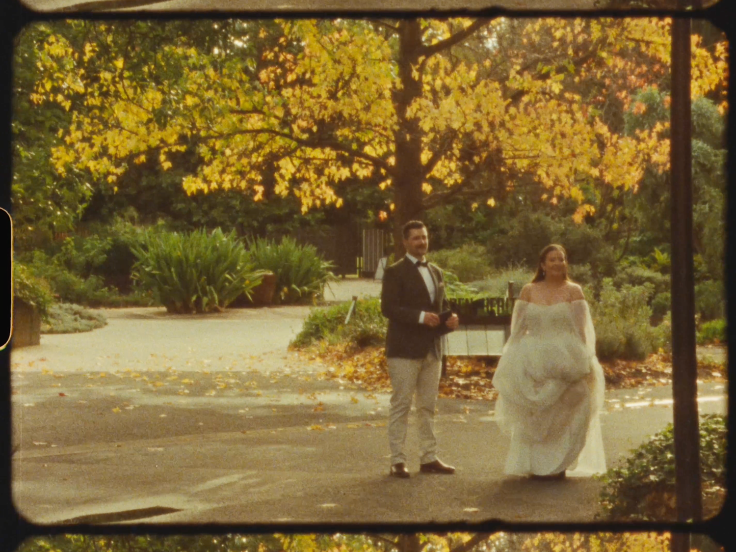 Bride and groom stand together in a park with vibrant autumn foliage during their outdoor wedding photoshoot.