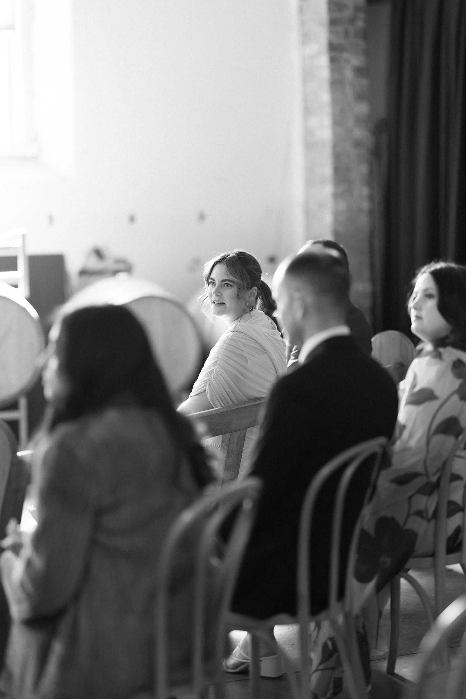 Black and white photo of wedding guests seated in chairs at an industrial venue ceremony.