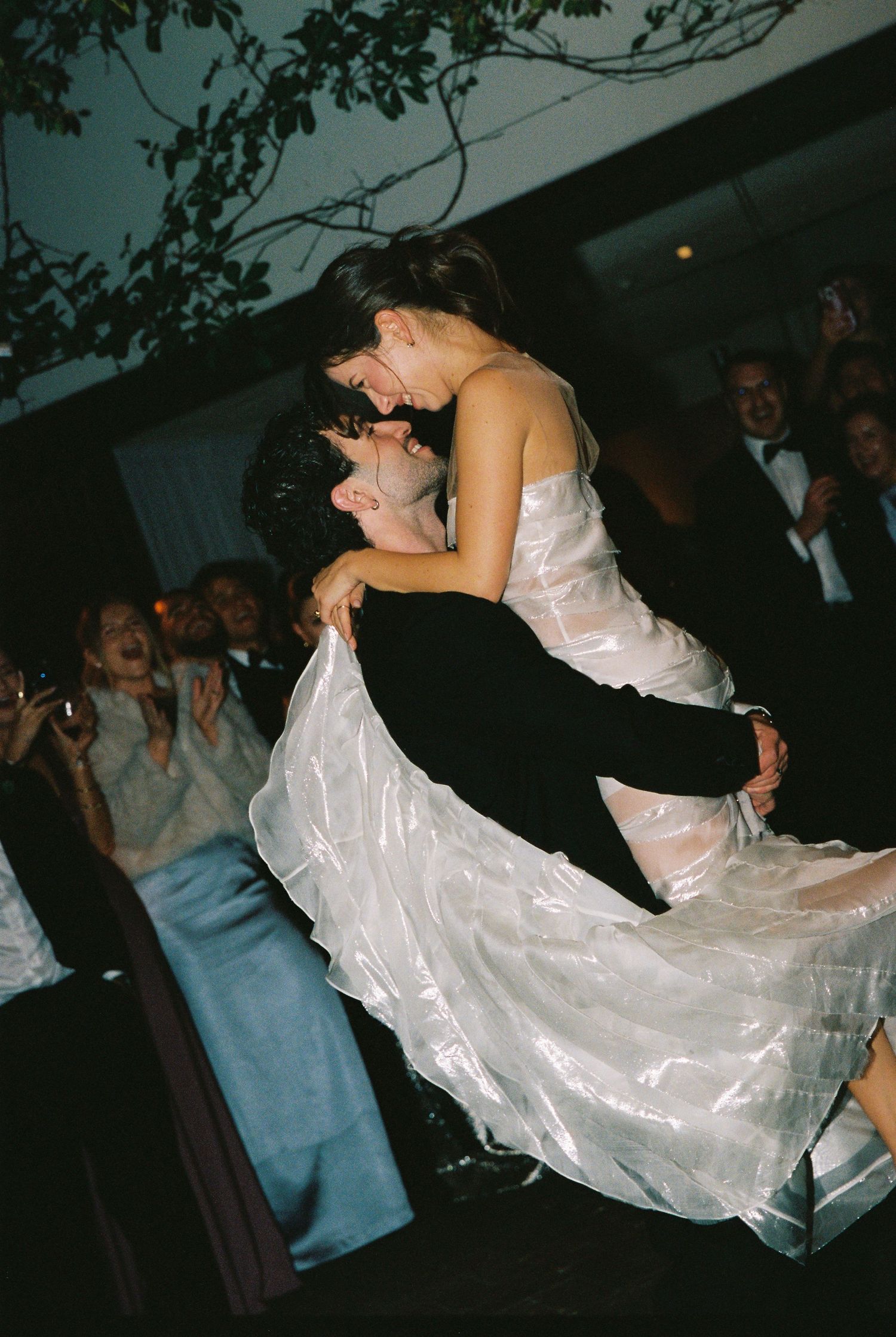 Groom lifting bride in a flowing white wedding dress during first dance at outdoor reception.