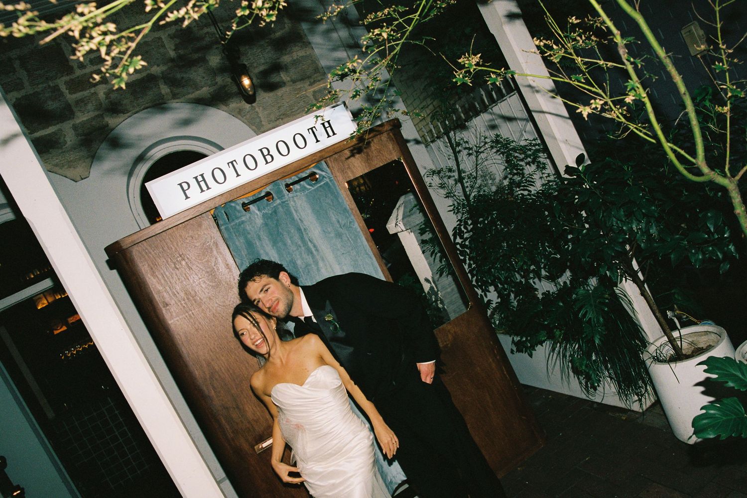 Bride and groom posing together outside a photobooth at their wedding reception.