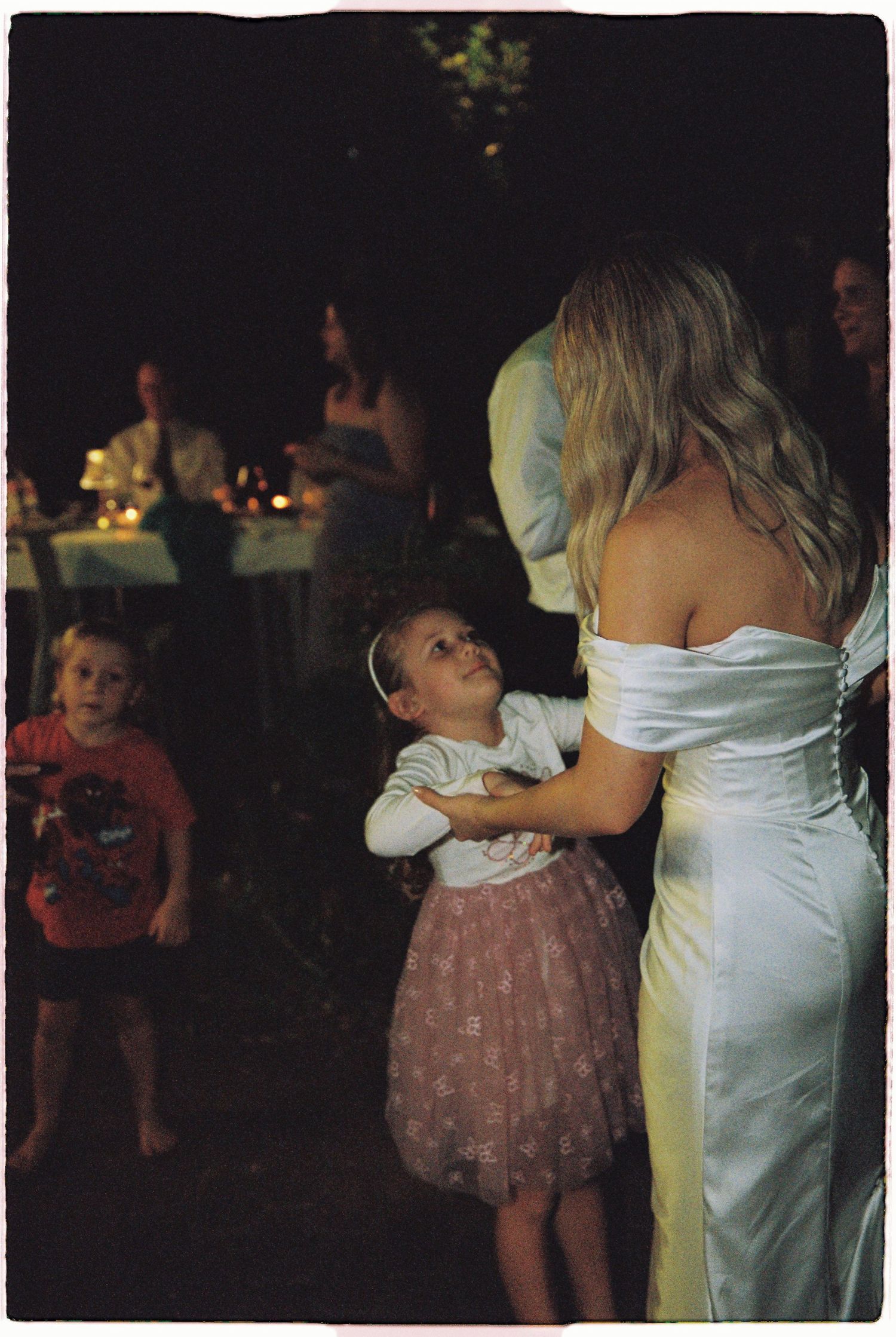 Sweet moment of young flower girl in pink tutu hugging the bride in white gown at wedding.
