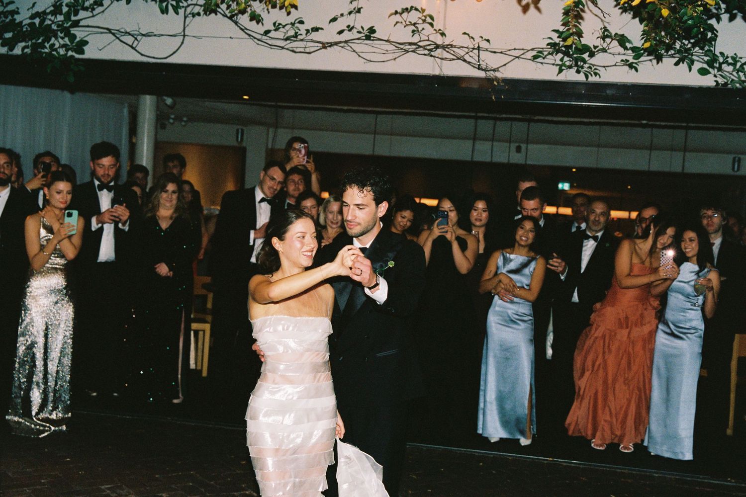 Bride and groom share their first dance outdoors at elegant wedding reception with applauding guests.