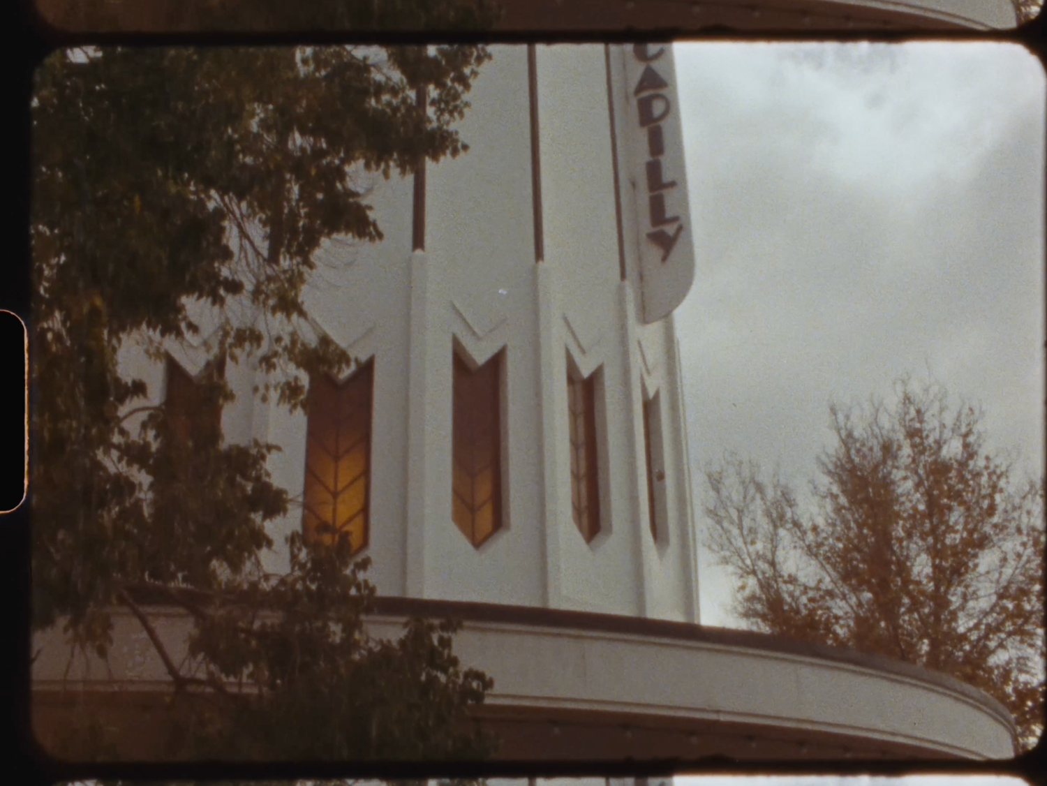 Art deco cinema facade with decorative stained glass windows and vertical signage against cloudy sky.