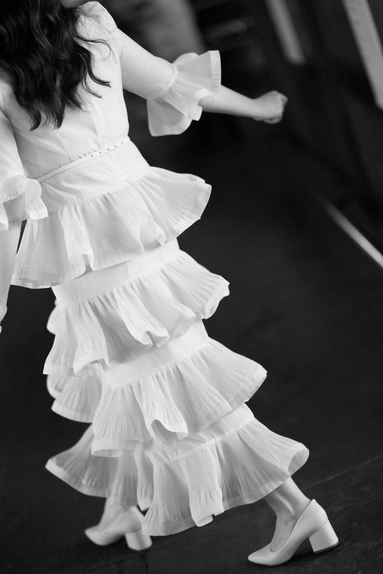 Black and white photo of bride twirling in tiered ruffled white wedding dress and block heels.