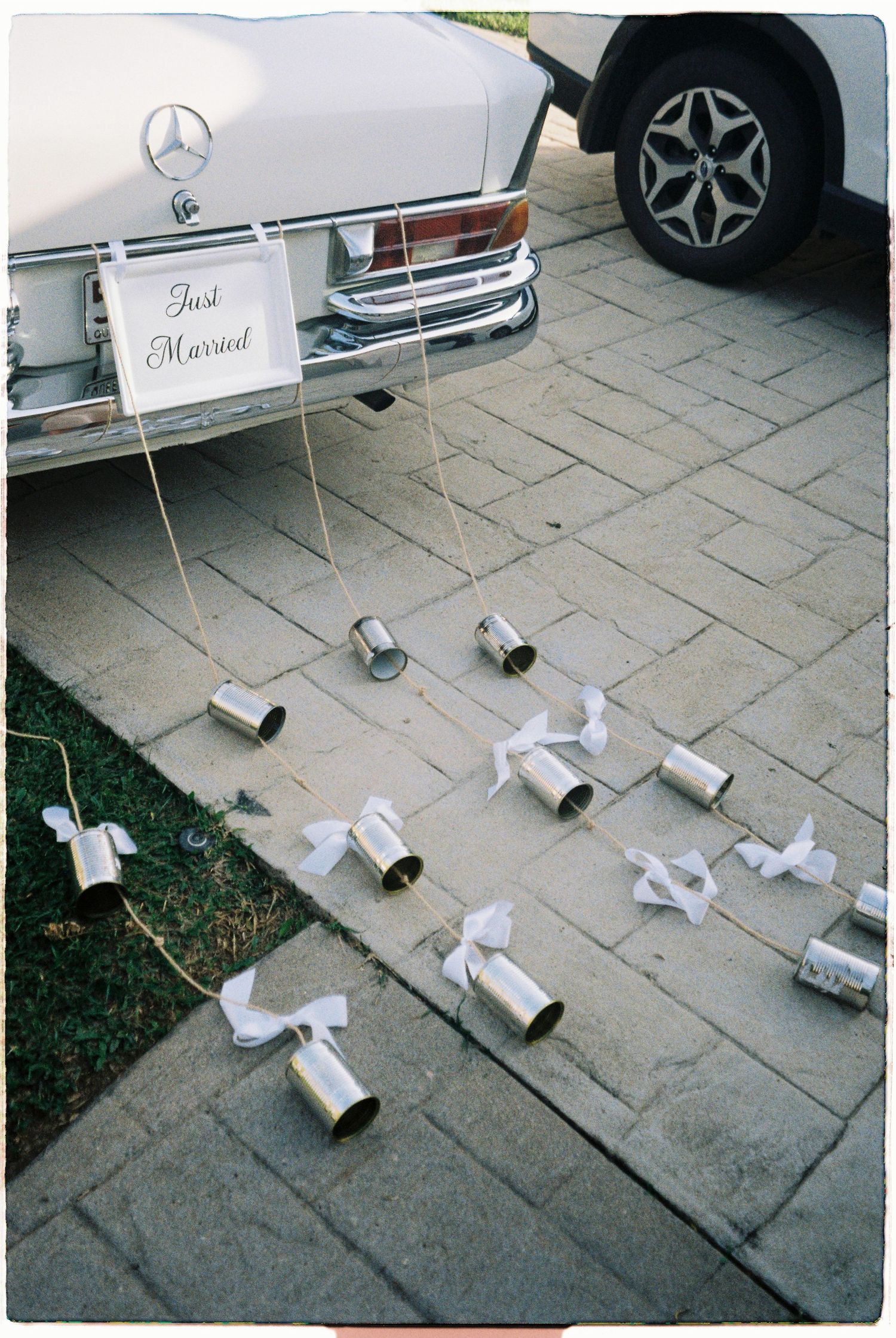 Classic white Mercedes decorated with tin cans and Just Married sign at wedding.