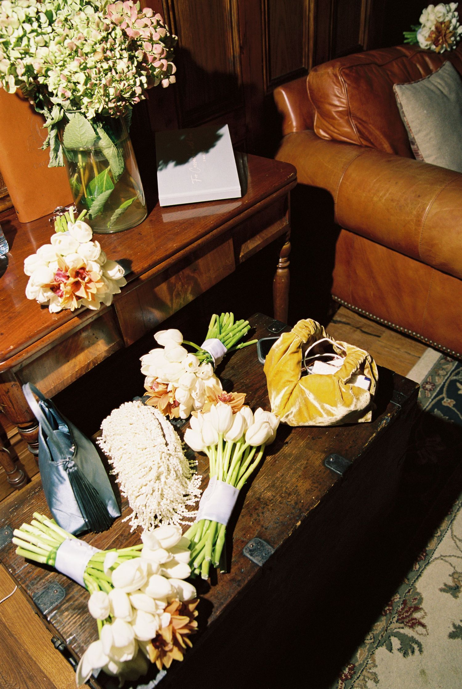 Wedding bouquets of white tulips and flowers arranged on a rustic wooden chest near a leather sofa.