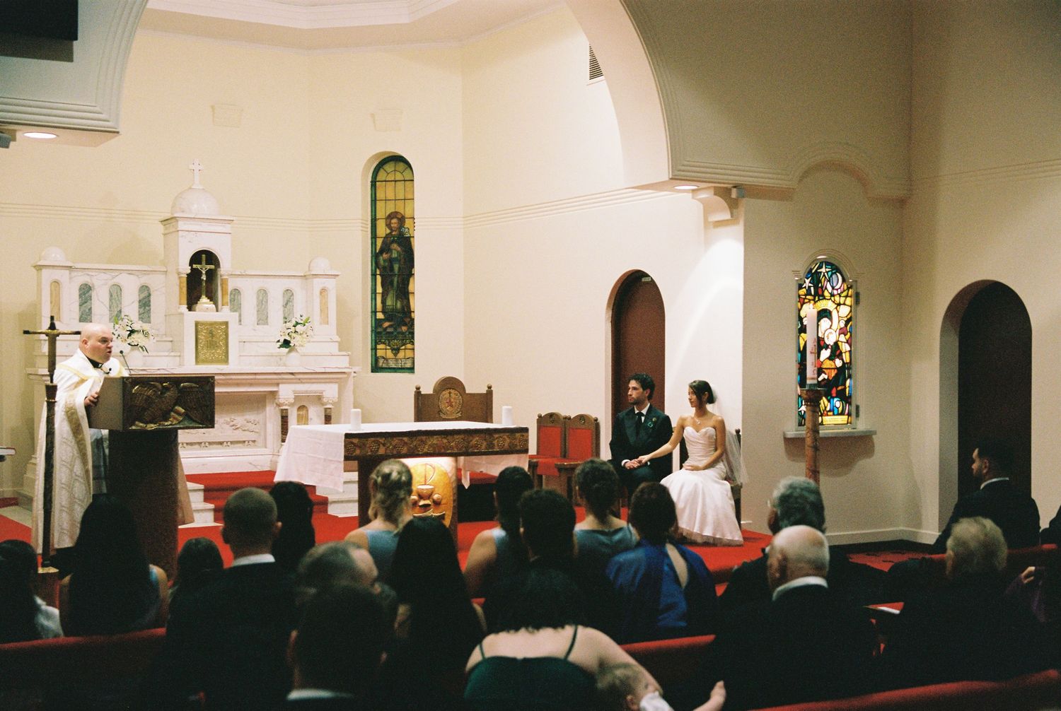 Bride and groom stand at altar during intimate church wedding ceremony with guests seated in pews.