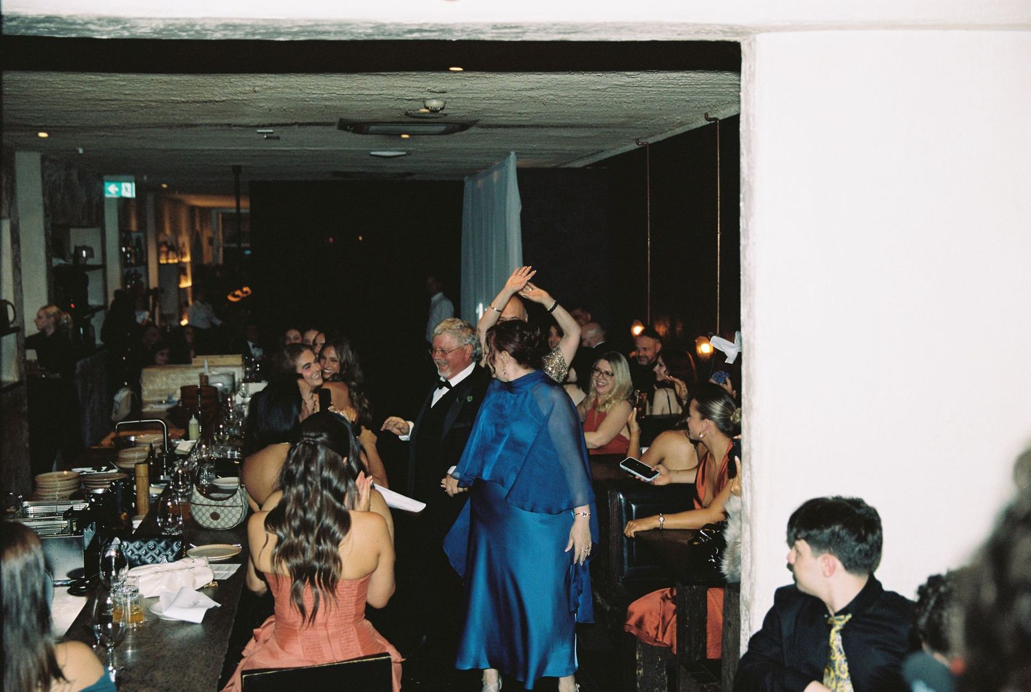 Wedding guests dancing and celebrating on dimly lit reception dance floor.