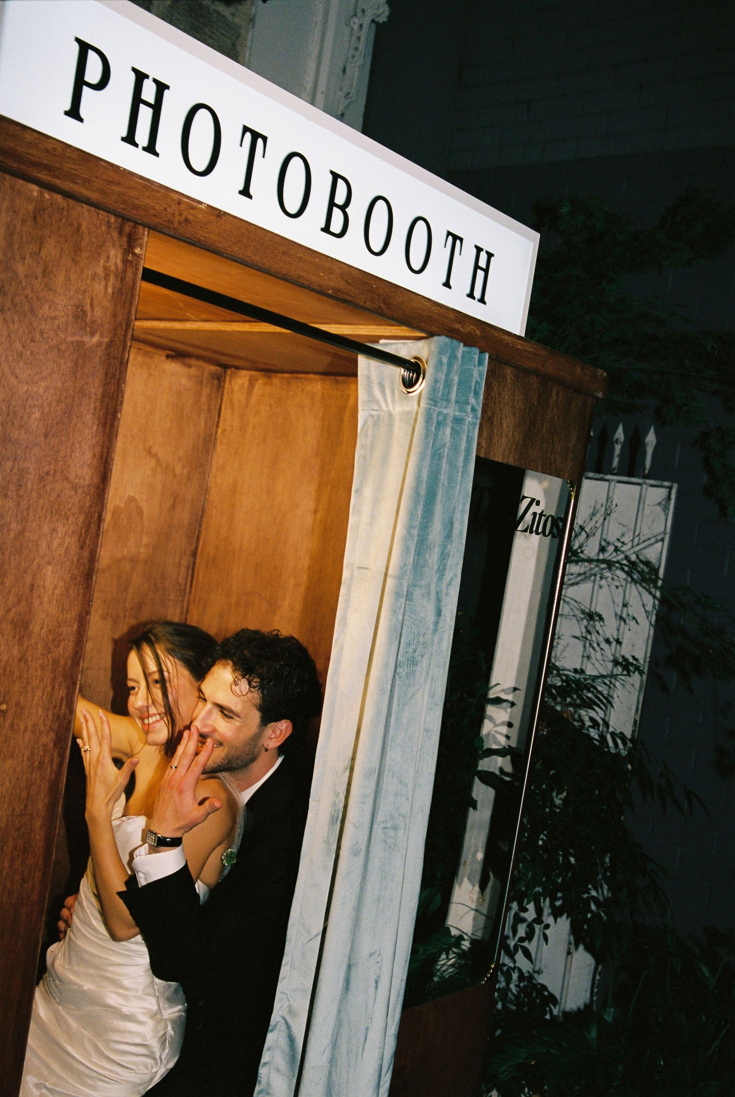 Couple sharing a romantic moment in a wooden photobooth at a wedding reception.