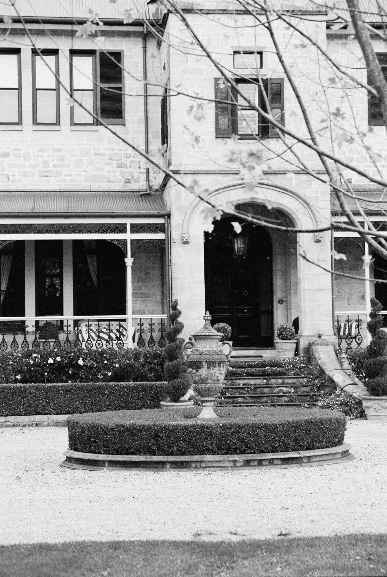 Black and white photo of elegant historic stone manor house with manicured hedges and ornamental urn.