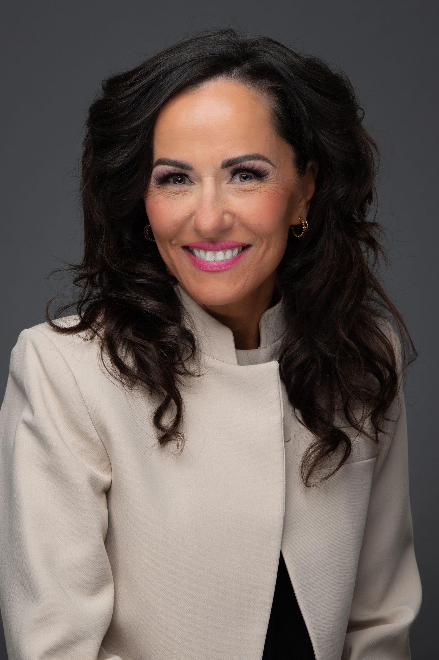 Professional headshot of a smiling dark-haired woman in a cream blazer.