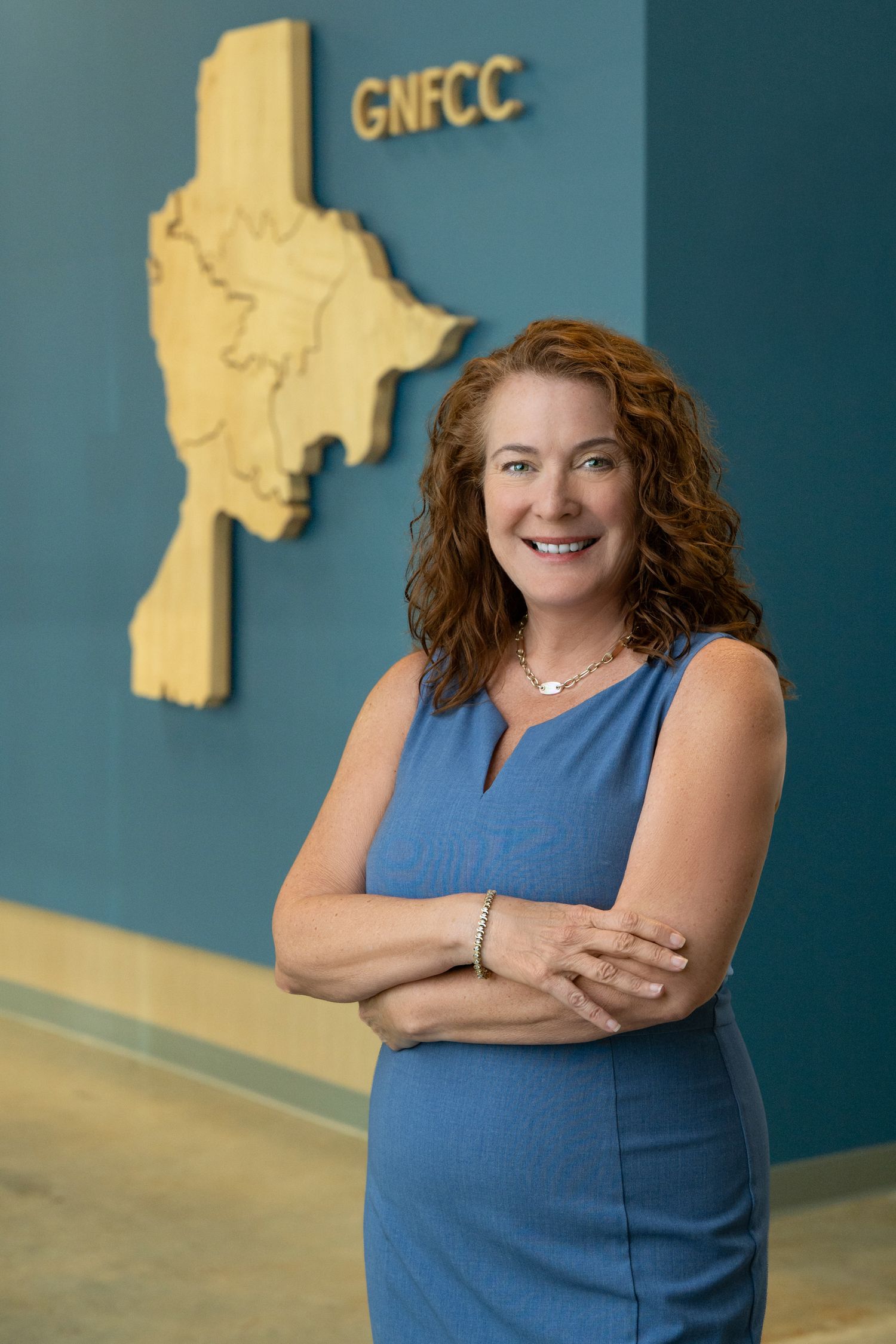 Professional woman with red curly hair smiling confidently in front of GNFCC logo wall display.