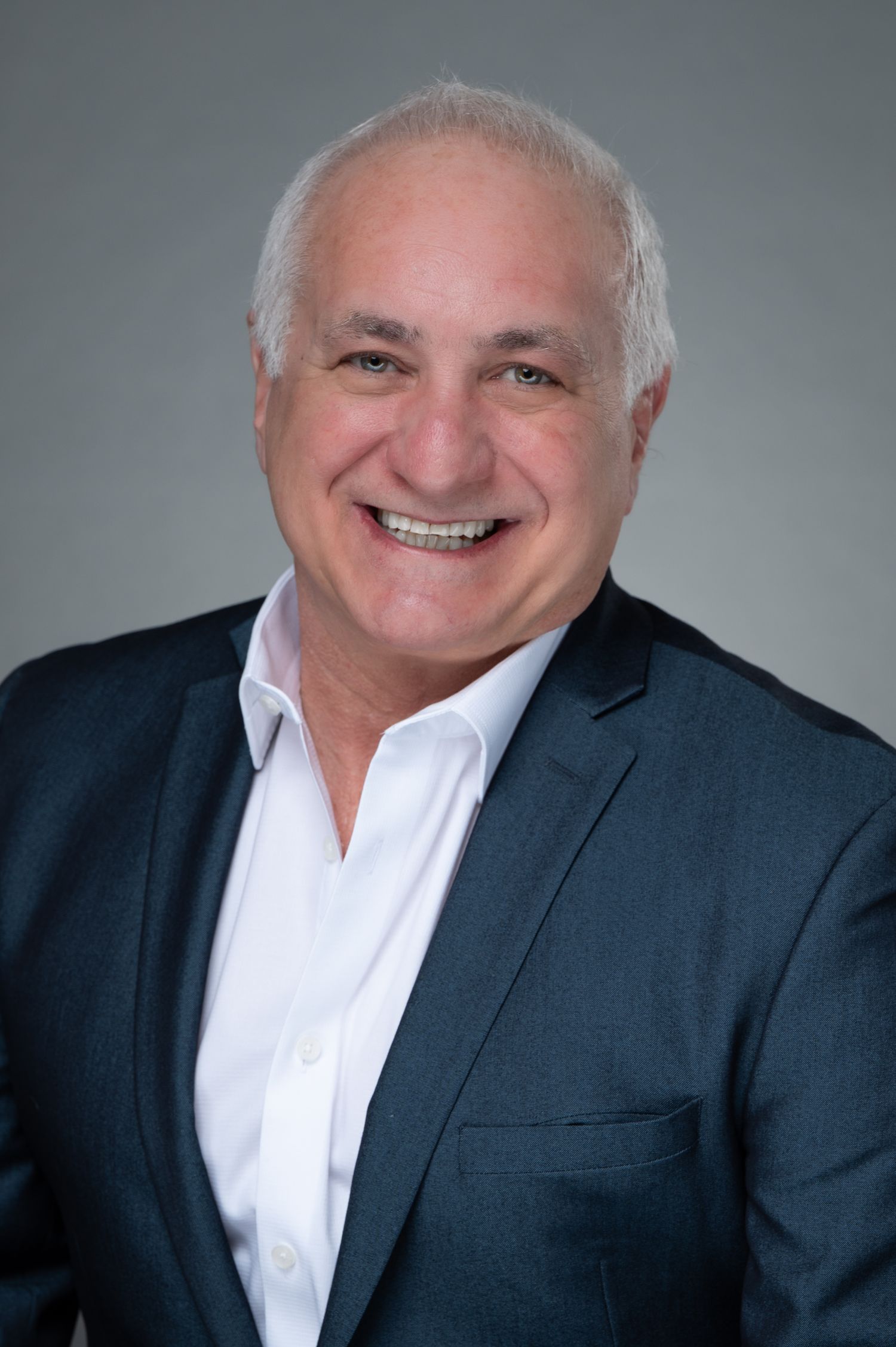 Friendly man with gray hair in a navy blazer smiling in a professional business headshot.