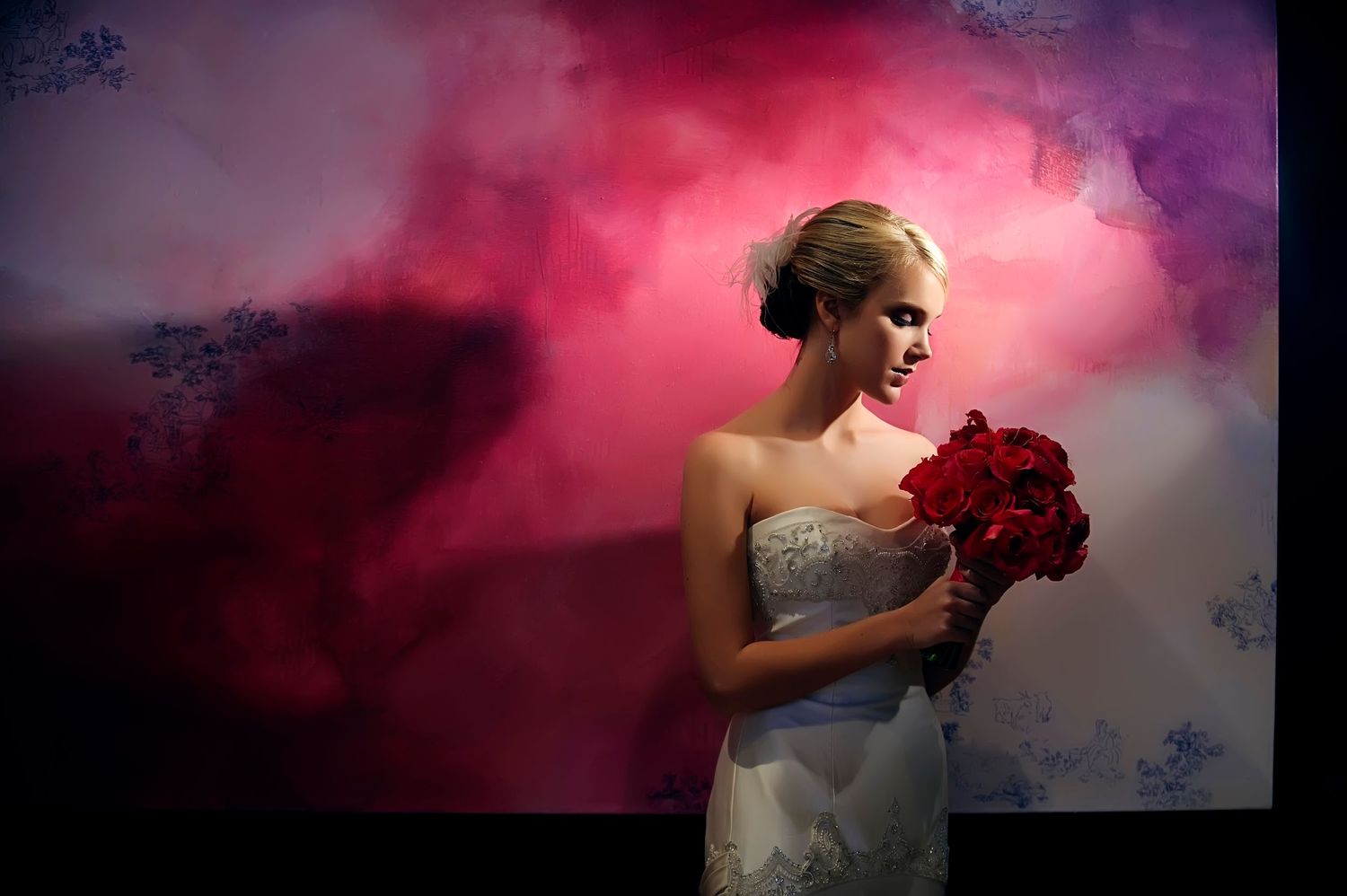Bride in strapless gown holding red bouquet against dramatic pink and purple smoke backdrop.
