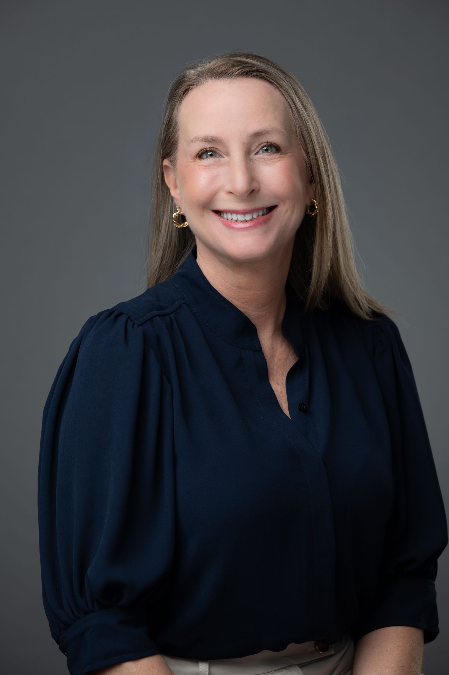 Professional headshot of a smiling woman with blonde hair wearing a navy blue blouse.