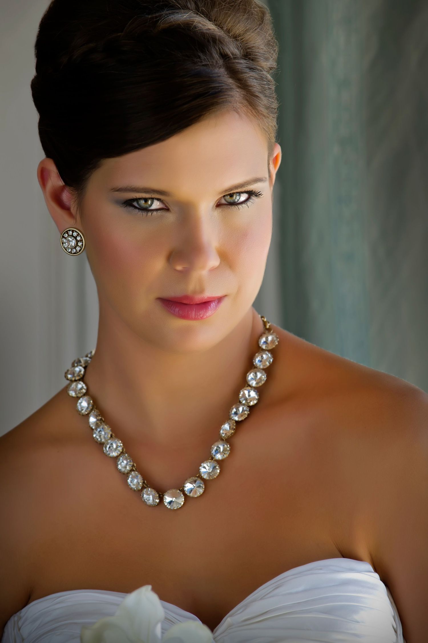 Bride wearing a sparkling crystal necklace and earrings with a strapless white dress, elegant updo hairstyle and bridal makeup.