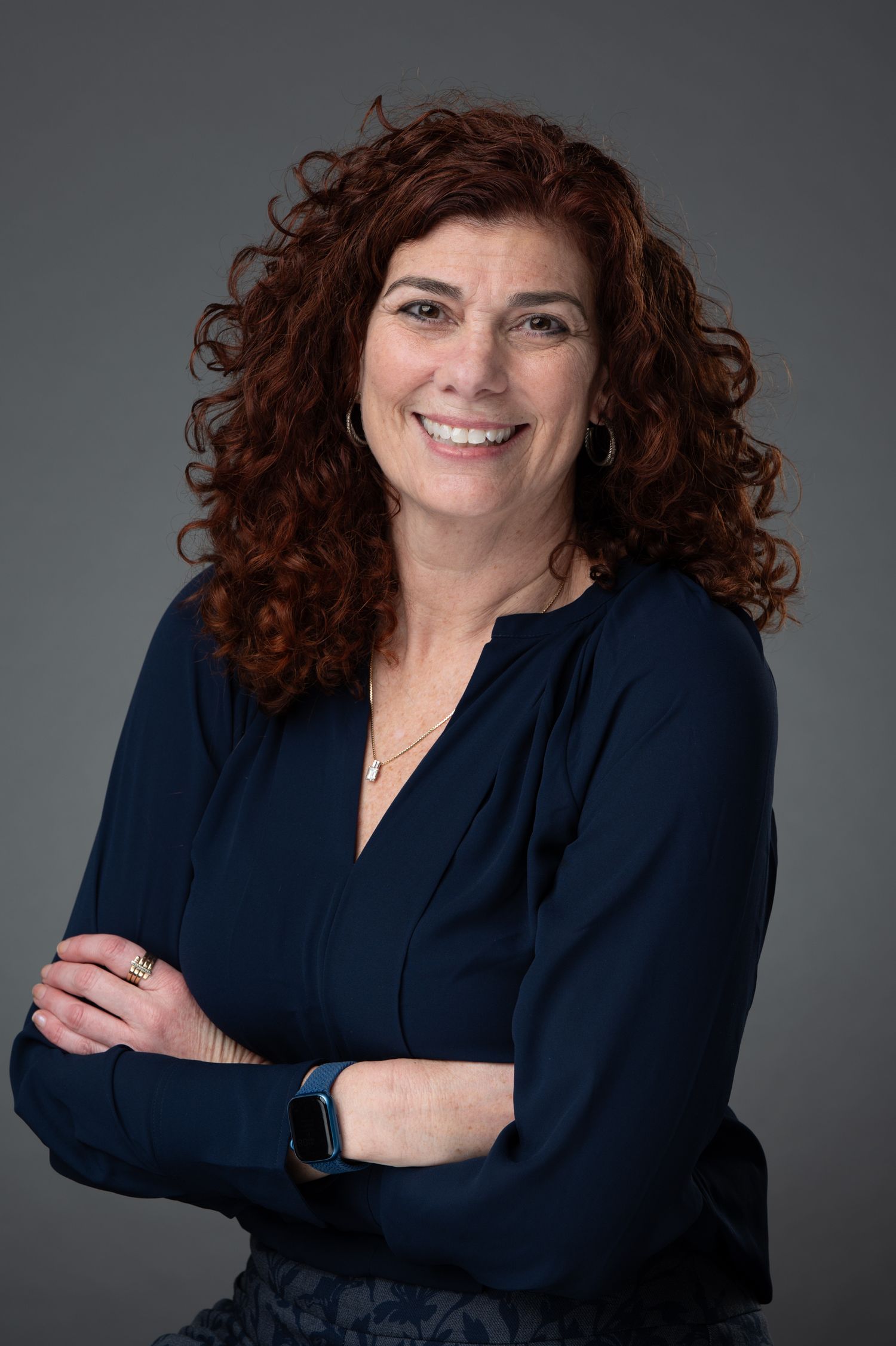 Professional woman with curly red hair smiling warmly for corporate headshot photo.