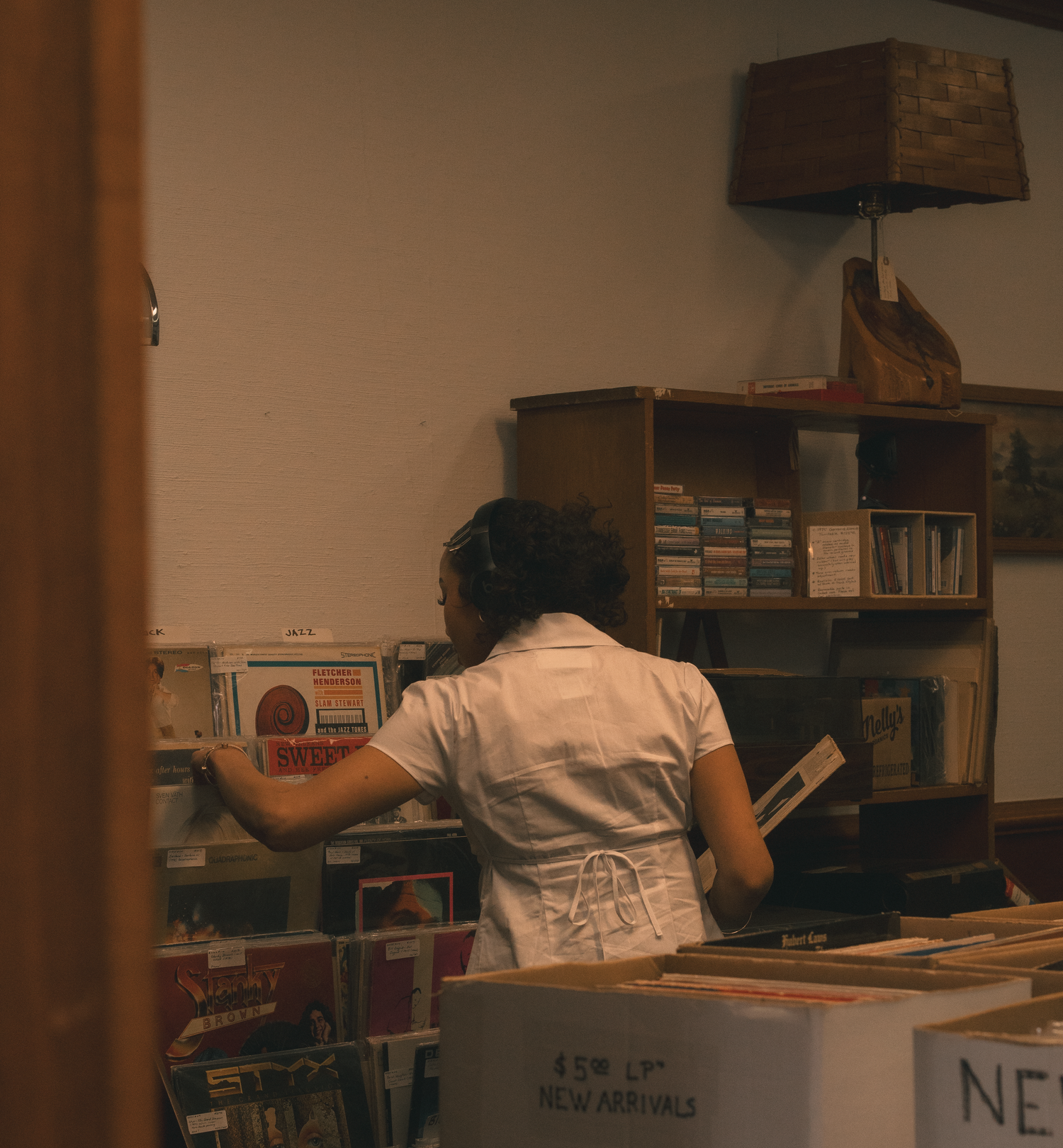 Woman browsing shelves of vinyl records and music items in a small record shop.