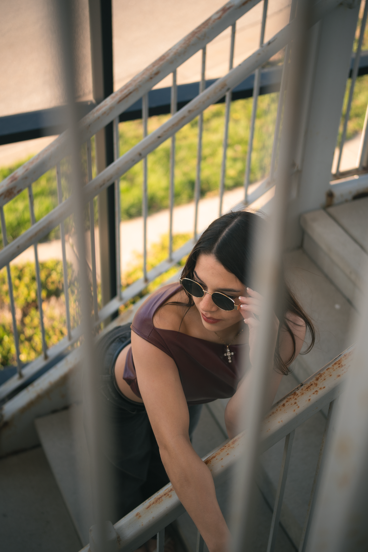 Young woman in sunglasses and purple crop top posing on metal staircase outdoors.