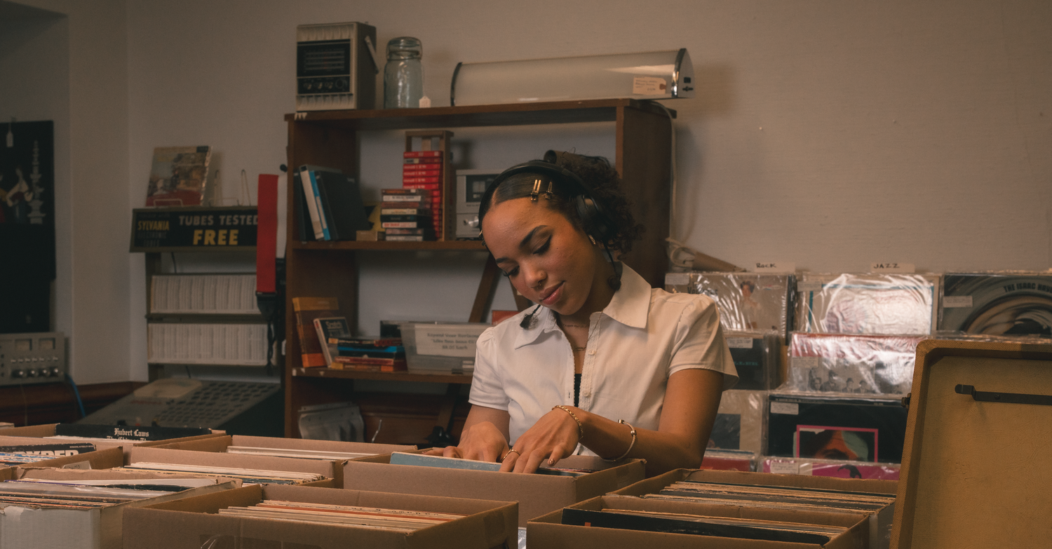 Young woman browsing vinyl records in a cozy music shop with bookshelves in the background.