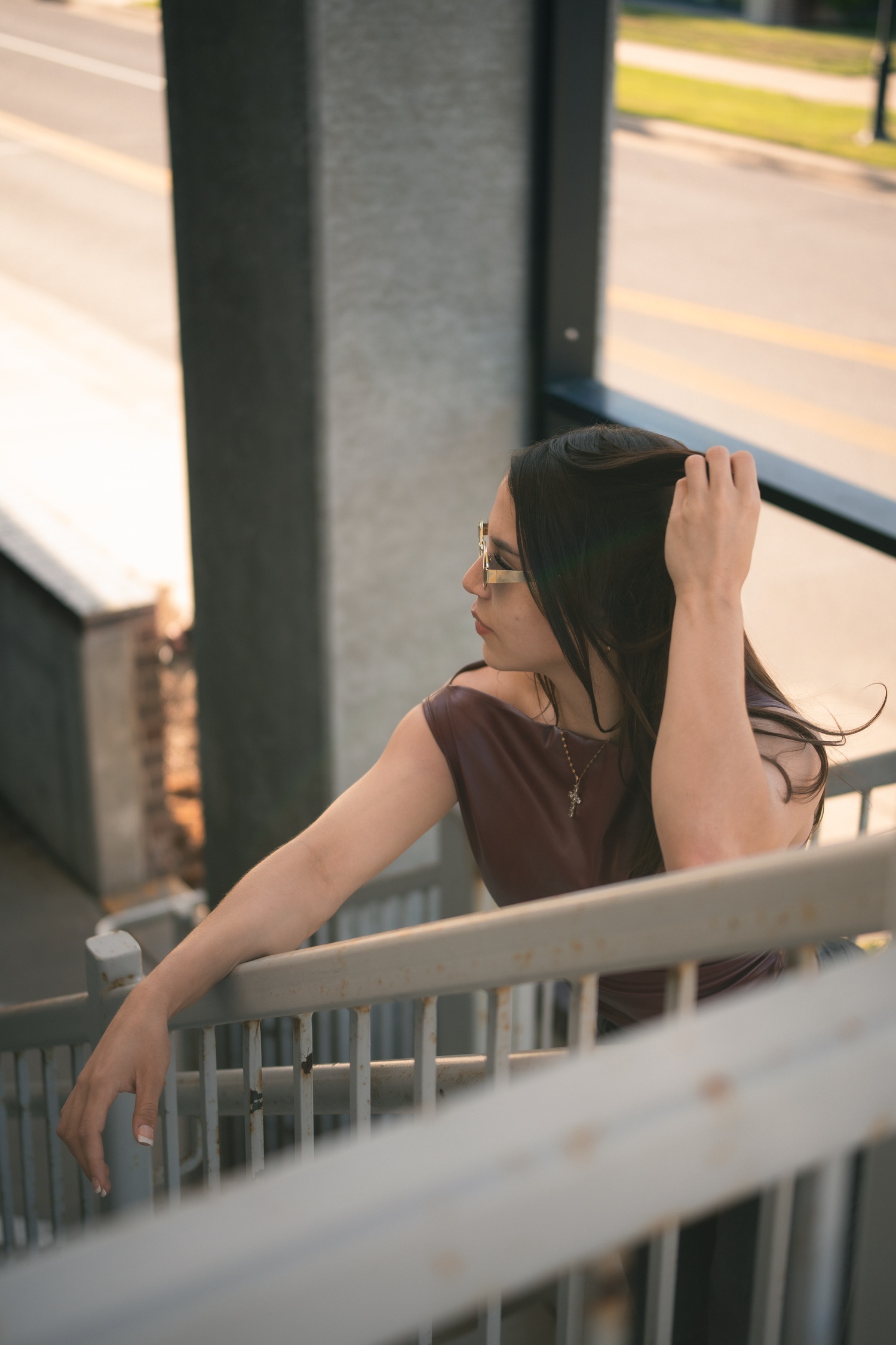 Young woman with glasses and cross necklace posing on staircase railing at sunset.