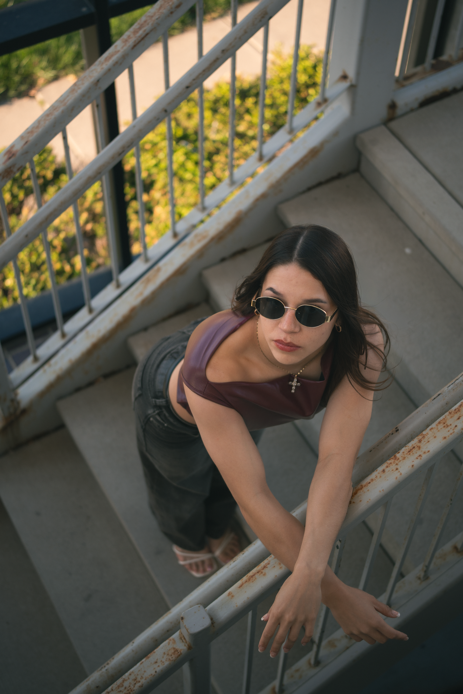 Young woman in sunglasses leaning on staircase railing outdoors in urban setting.