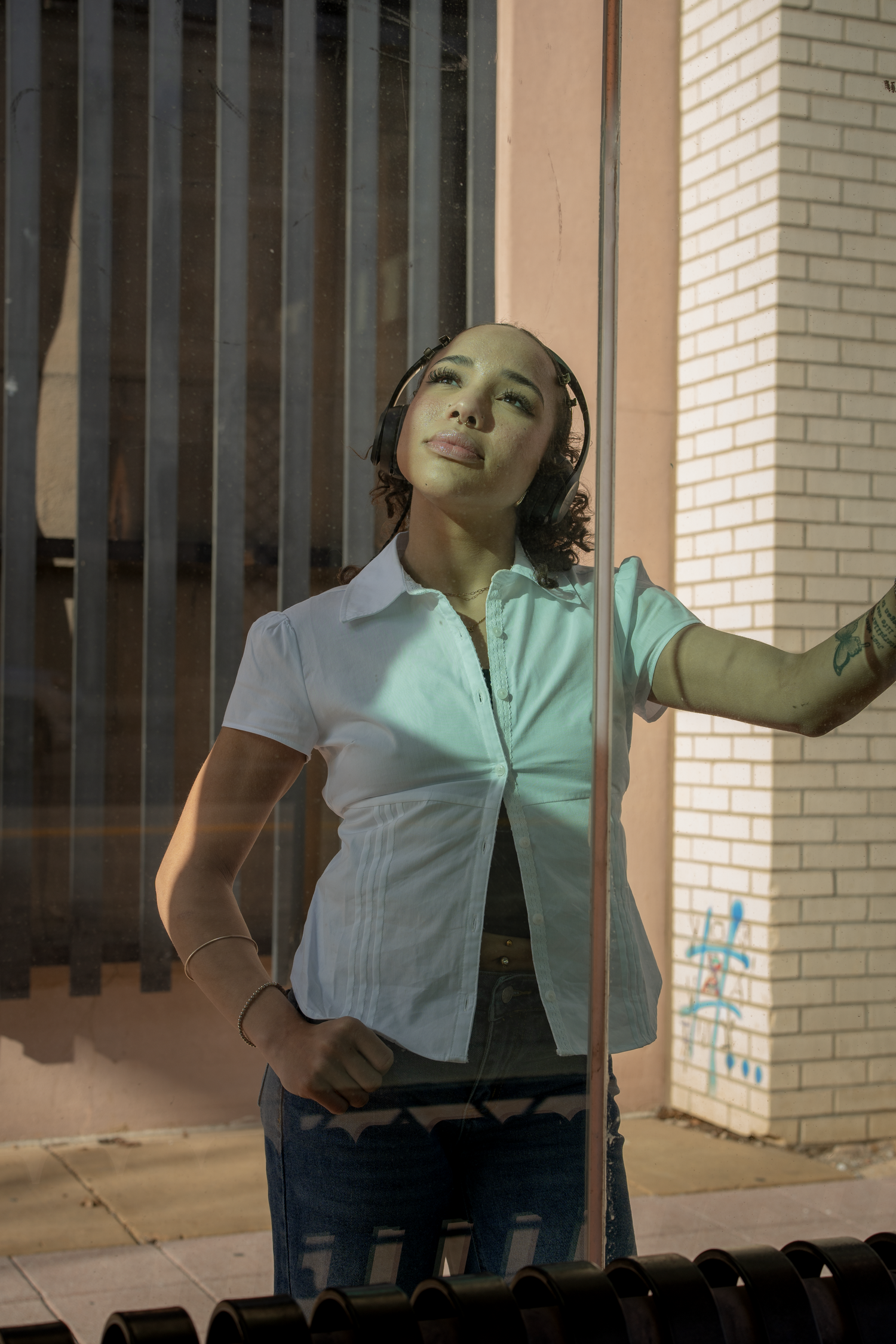 Young woman with headphones leaning against glass door of a record store exterior.