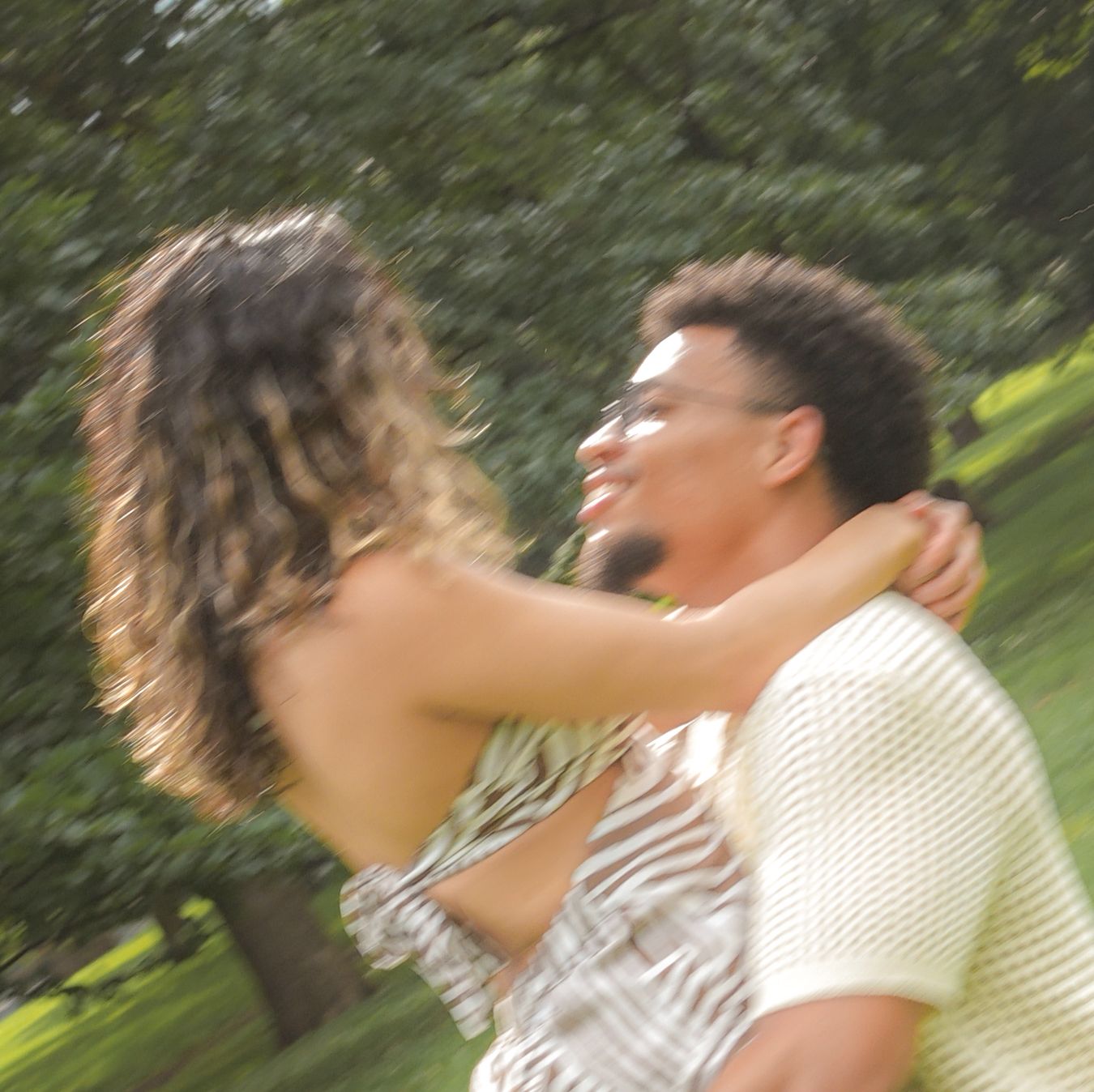 A joyful couple spinning and embracing outdoors in a park, captured with a dreamy motion blur effect.