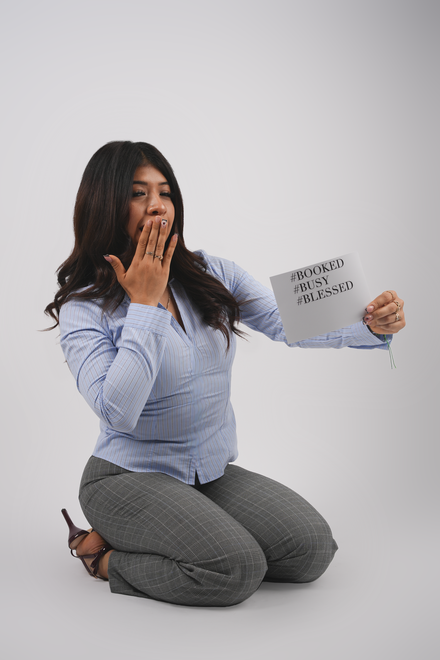 Woman kneeling on floor holding a sign reading #Booked #Busy #Blessed with hand over mouth in surprise.