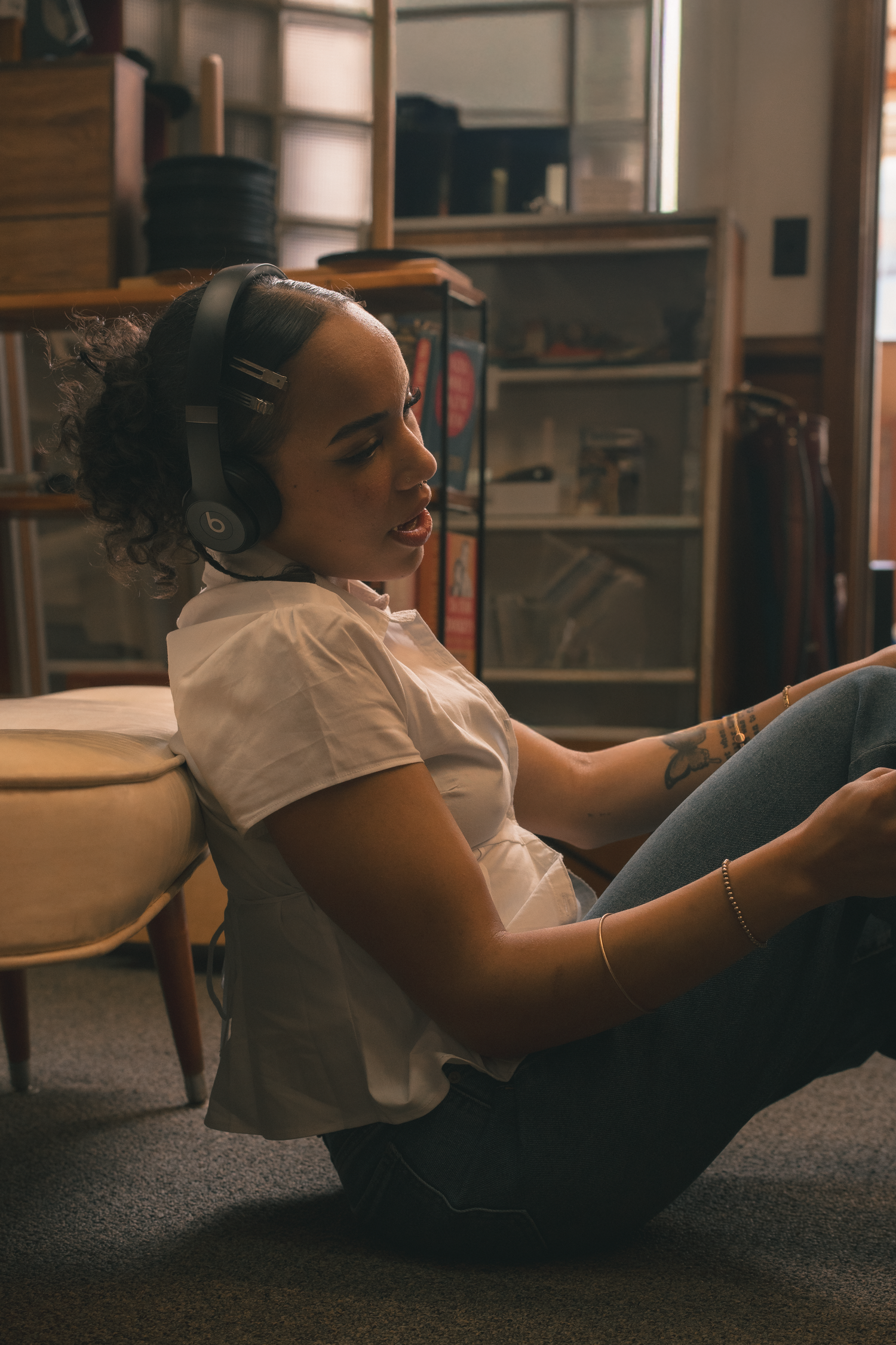 Young woman with headphones sitting on floor in a warmly lit vintage record shop.