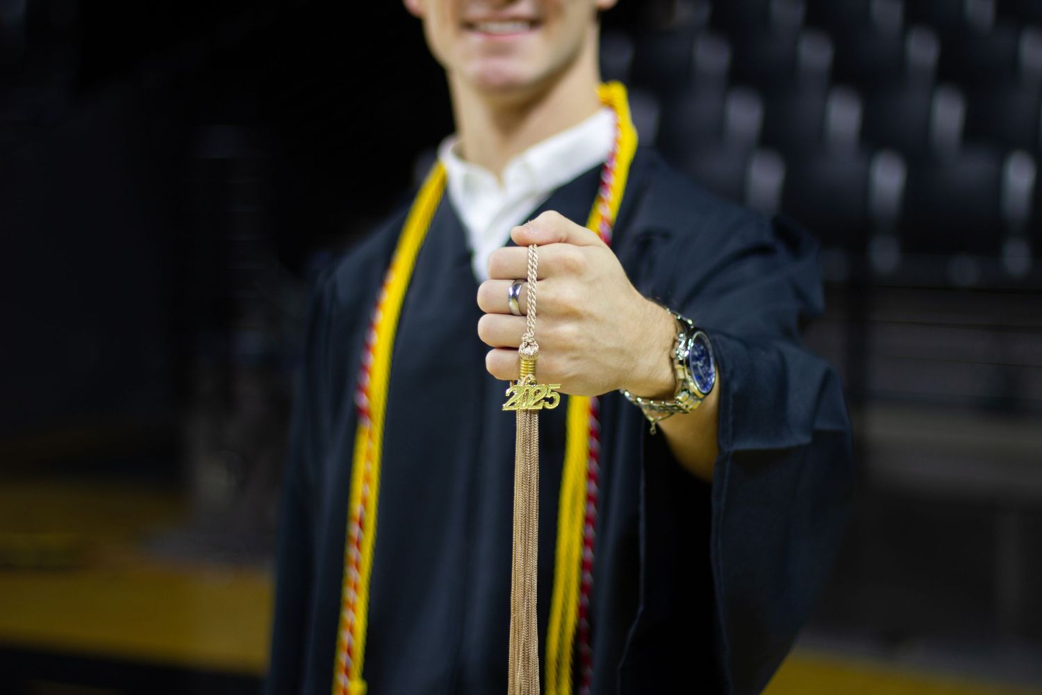 Close-up of graduate holding a 2025 tassel in a black graduation gown with gold and red stole.