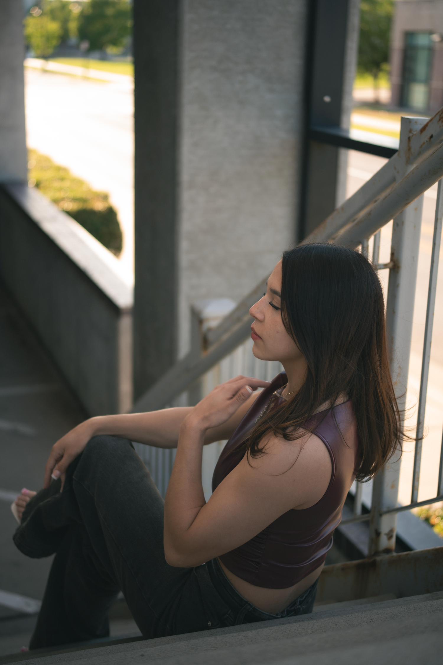 Young woman in purple crop top sits pensively on outdoor staircase in urban setting.