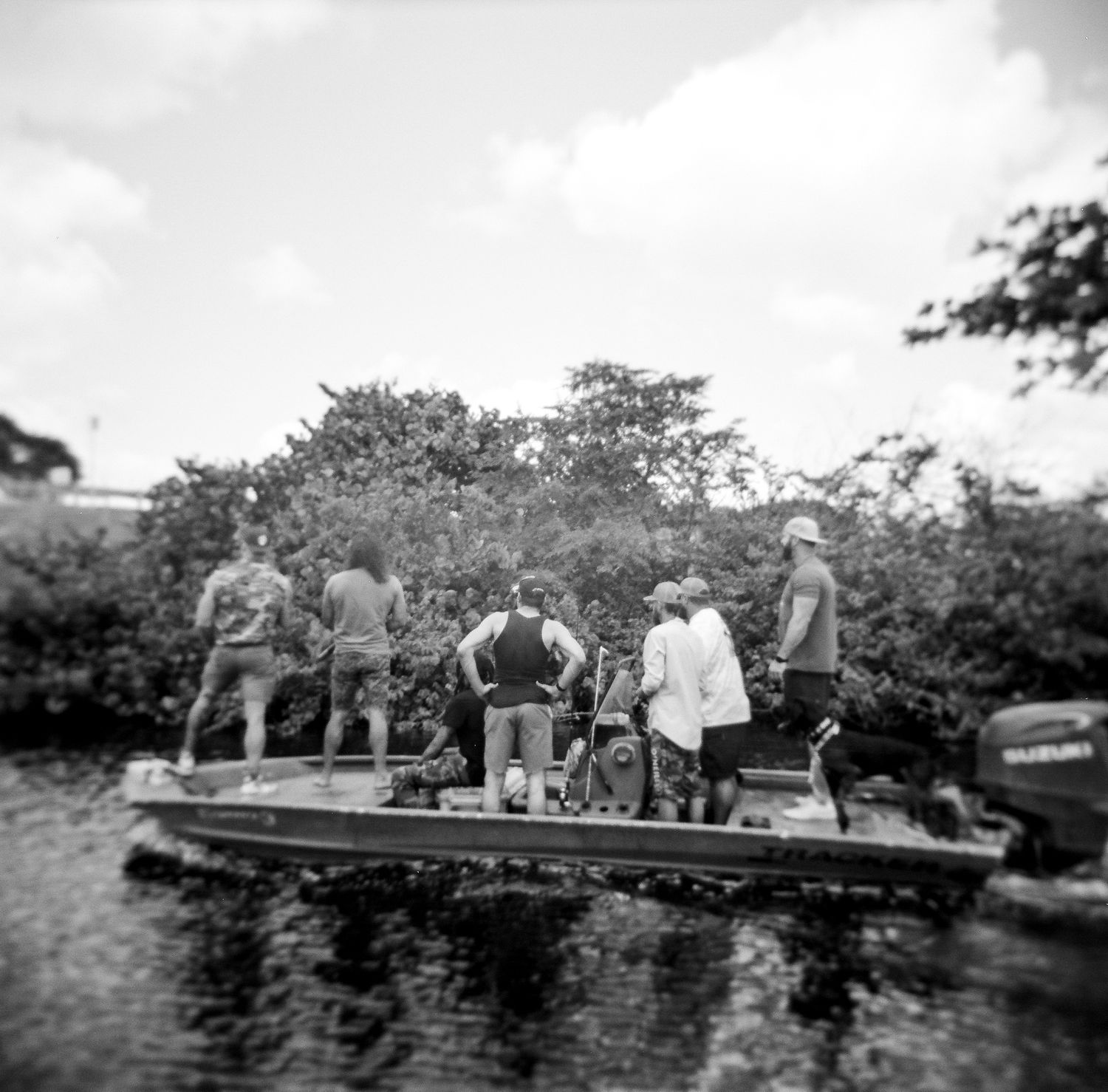Black and white photo of a group of people standing on a flat boat surrounded by lush green vegetation.