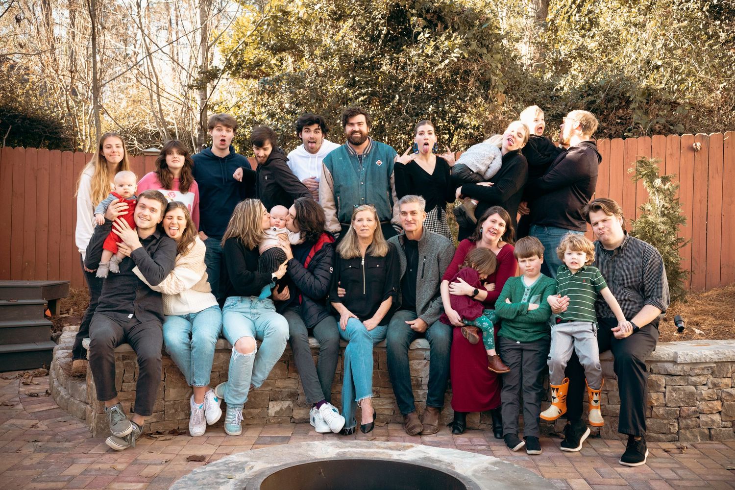 Large extended family posing together outdoors near a fire pit in a winter backyard.