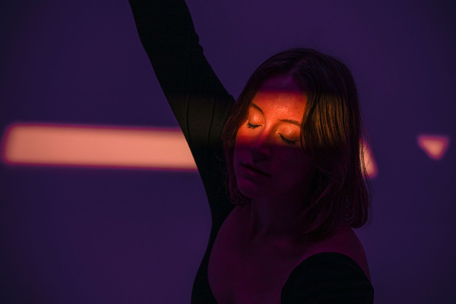 Woman with eyes closed raises arm under purple and orange stage lighting.