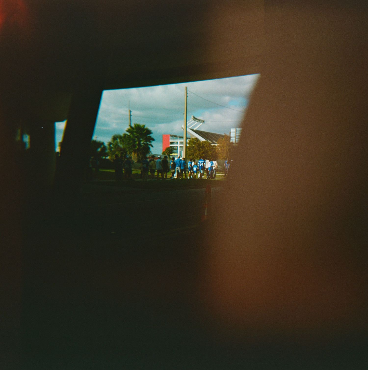 View through a car window of people gathering outside a stadium on a cloudy day.